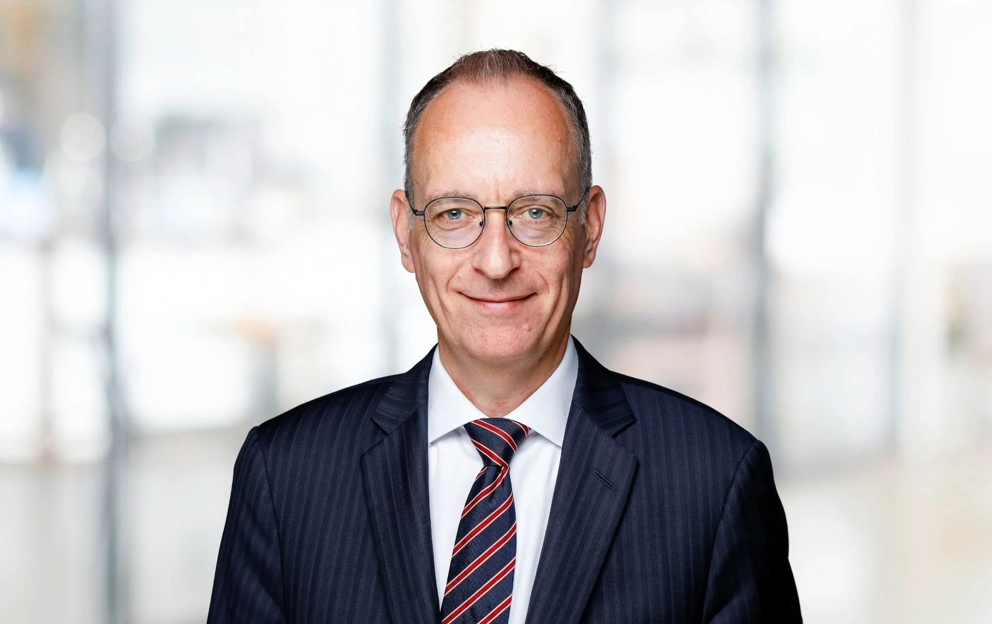 Porträt eines Mannes in Anzug und Krawatte vor unscharfem hellem Hintergrund.