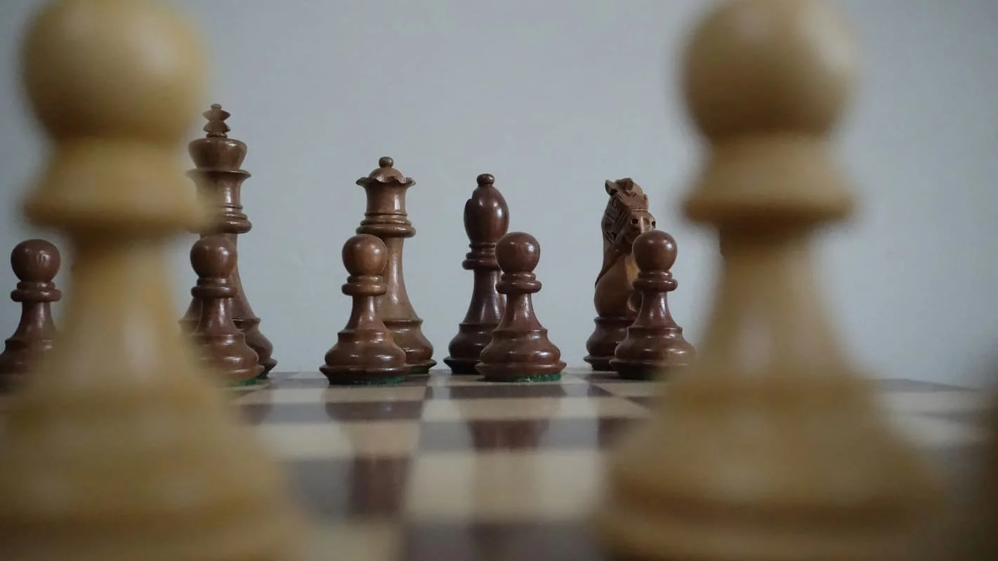 Nahaufnahme von hellbraunen und dunkelbraunen Schachfiguren vor einem Schachspiel