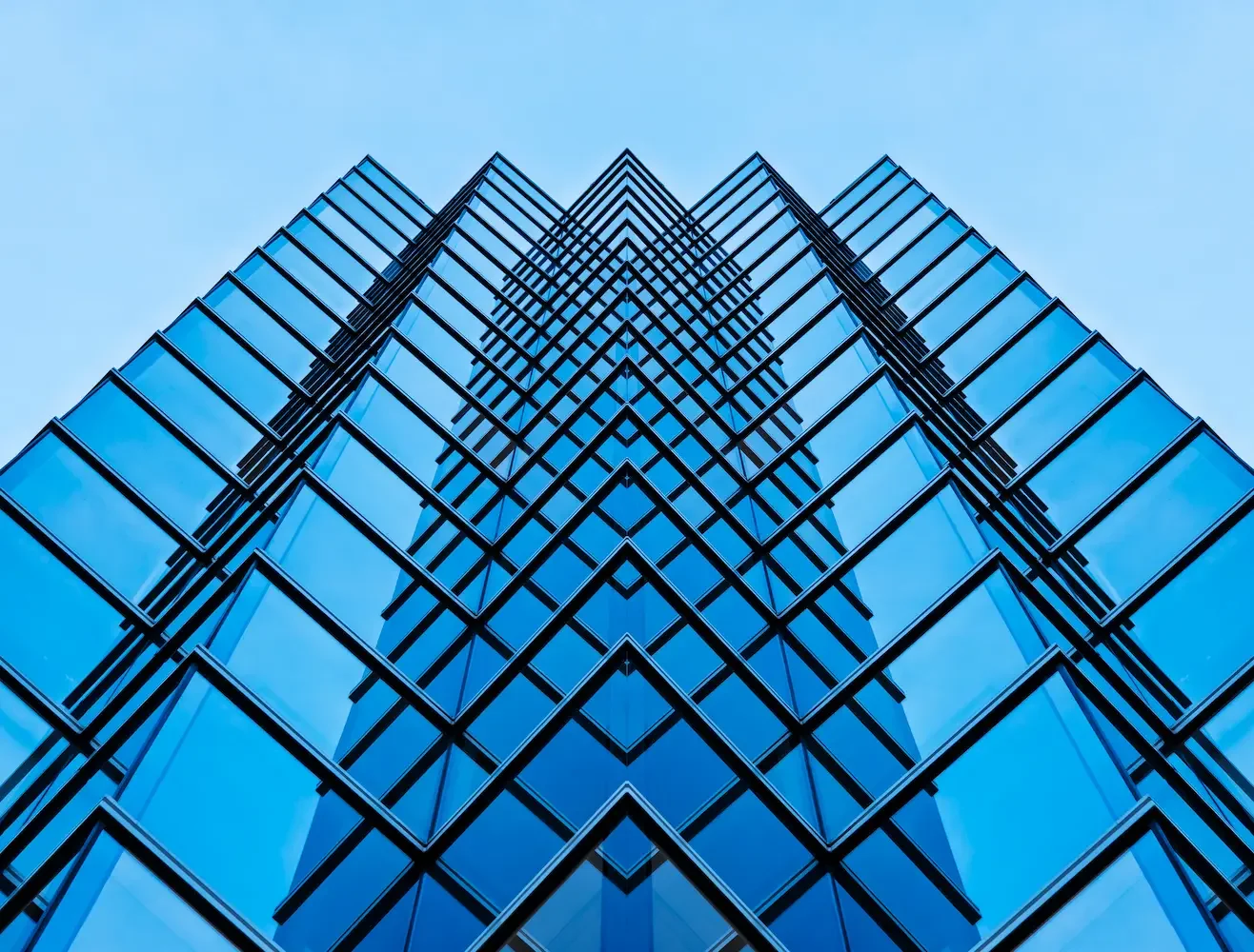 Aufnahme eines modernen Wolkenkratzers aus Glas, fotografiert von unten nach oben, mit Blick zur Spitze gegen einen blauen Himmel.