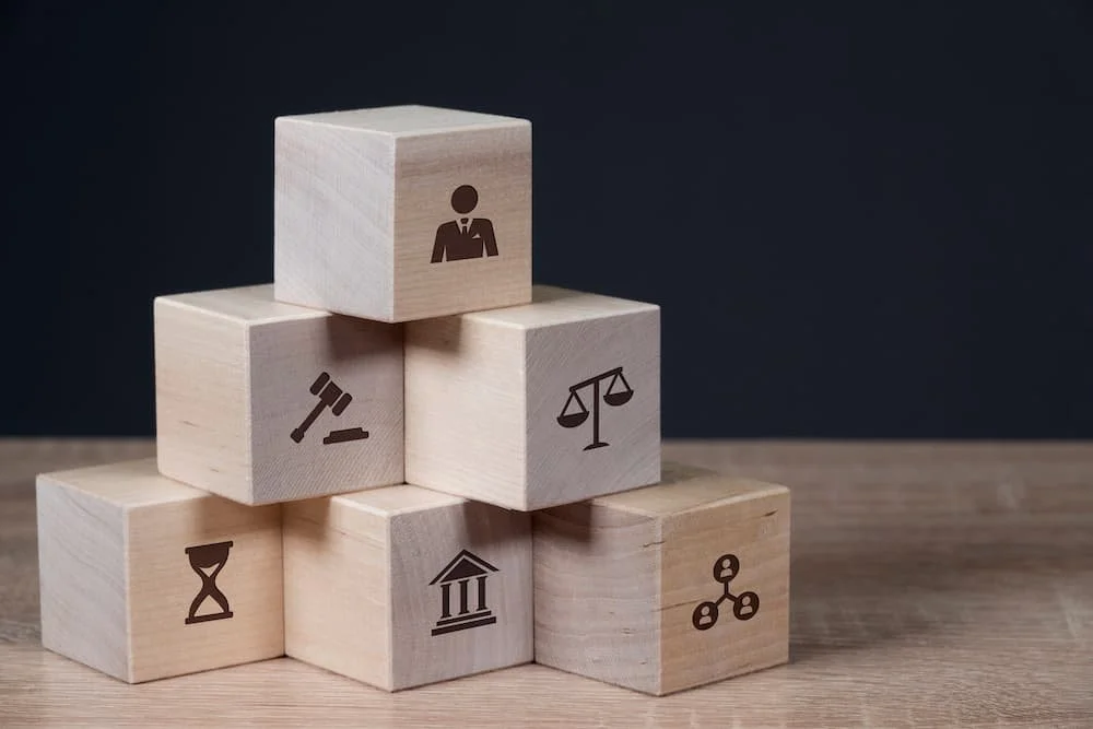 Holzbauklötze mit Symbolen für Recht, Bank, Hierarchie, Aktie, Gerechtigkeit, Zeit, Gavel, und Personalwirtschaft.