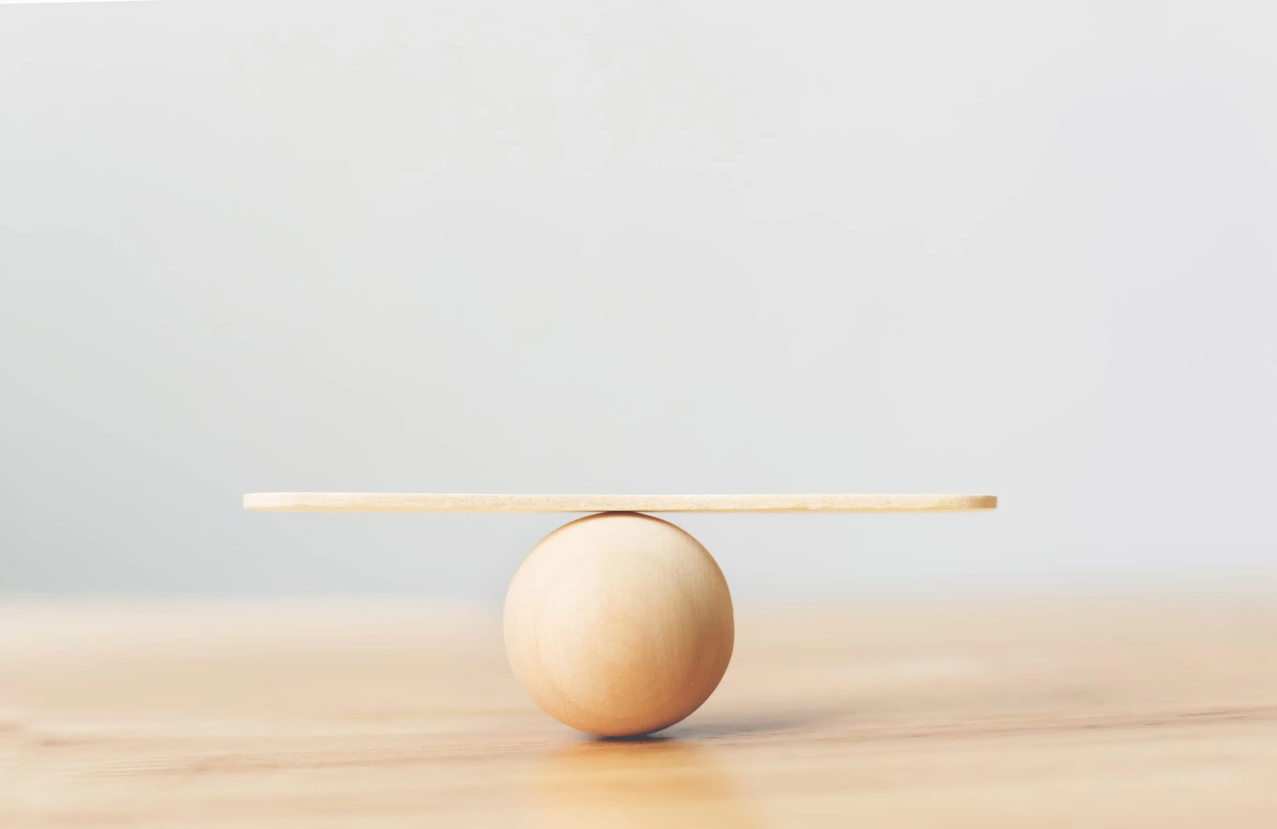 Holzkugel mit ausbalanciertem Brett als Symbol für den Balanceakt bei Restrukturierungen