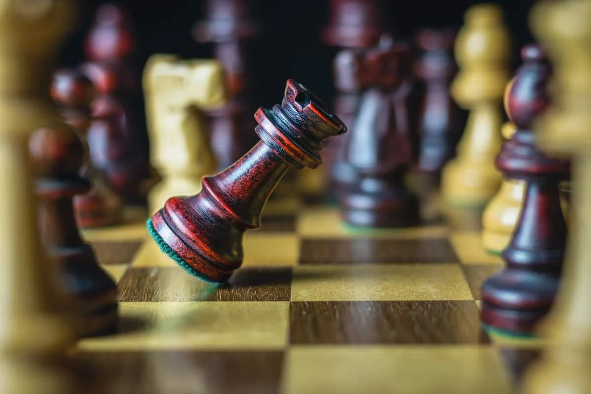 Ein Schachbrett mit einer umgefallenen schwarzen Spielfigur, umgeben von aufgestellten Figuren.