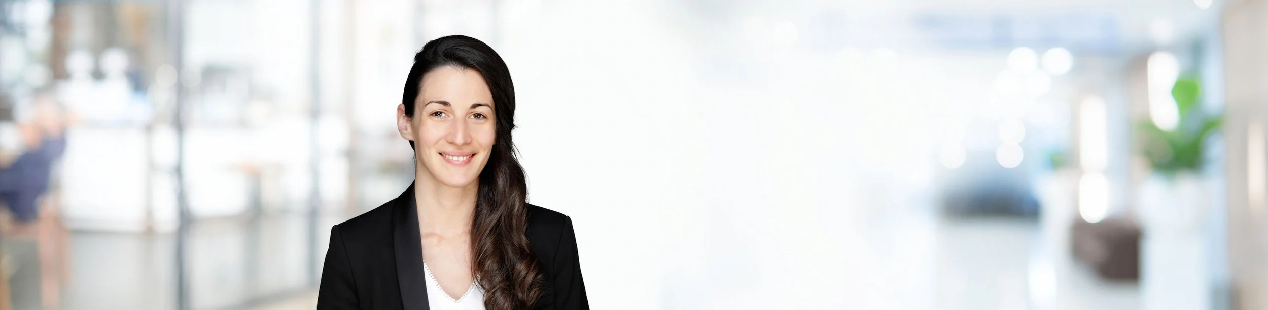 Porträt einer jungen Frau in dunklem Blazer vor hellem Hintergrund in einem modernen Raum.