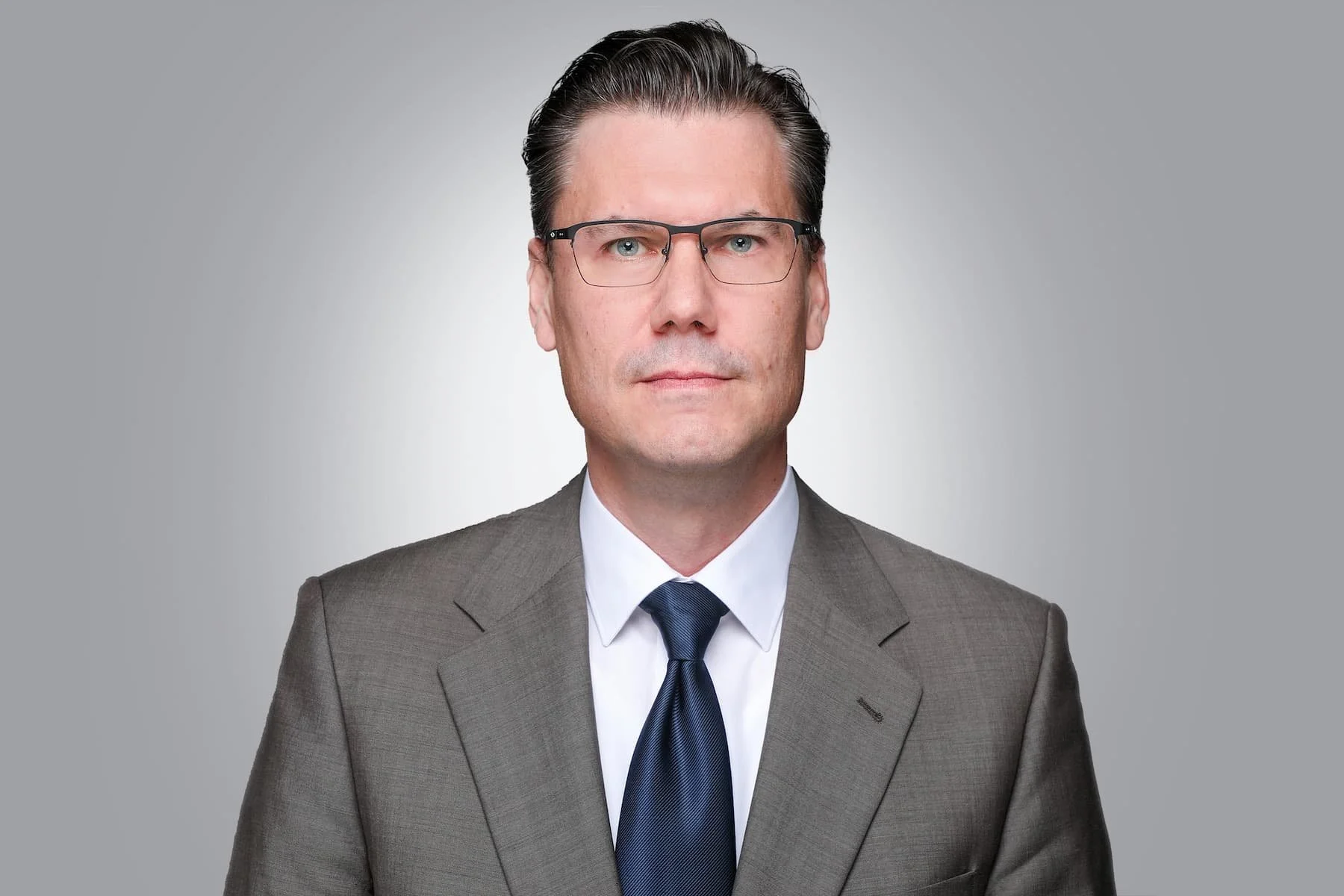 Porträt eines Rechtsanwalts im grauen Anzug mit Krawatte vor neutralem Hintergrund, seriöser Geschäftsstil.