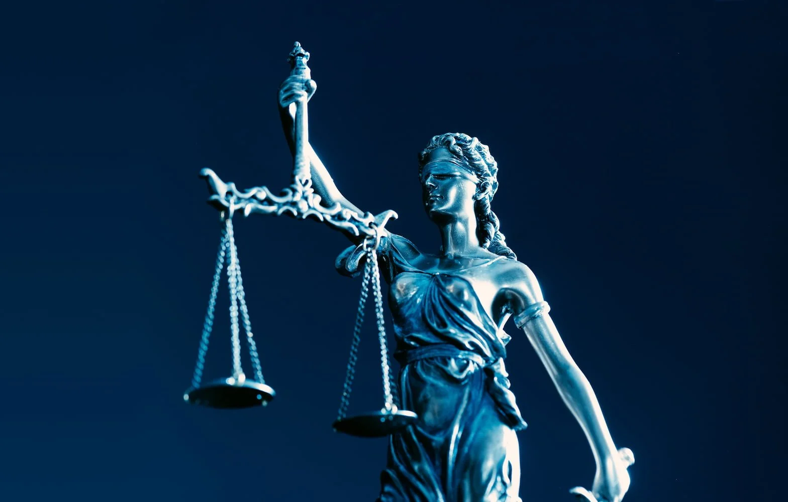 Eine Skulptur der Justitia mit verbundenen Augen, die eine Waage in einer Hand und ein Schwert in der anderen hält, symbolisiert Gerechtigkeit.