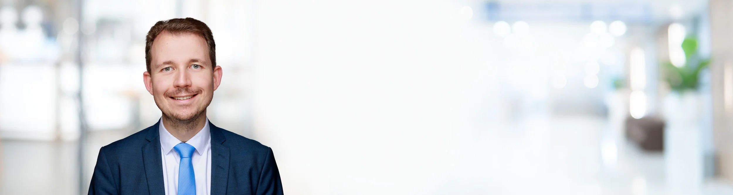 Porträt eines Mannes in Businesskleidung vor einem hellen, unscharfen Hintergrund.