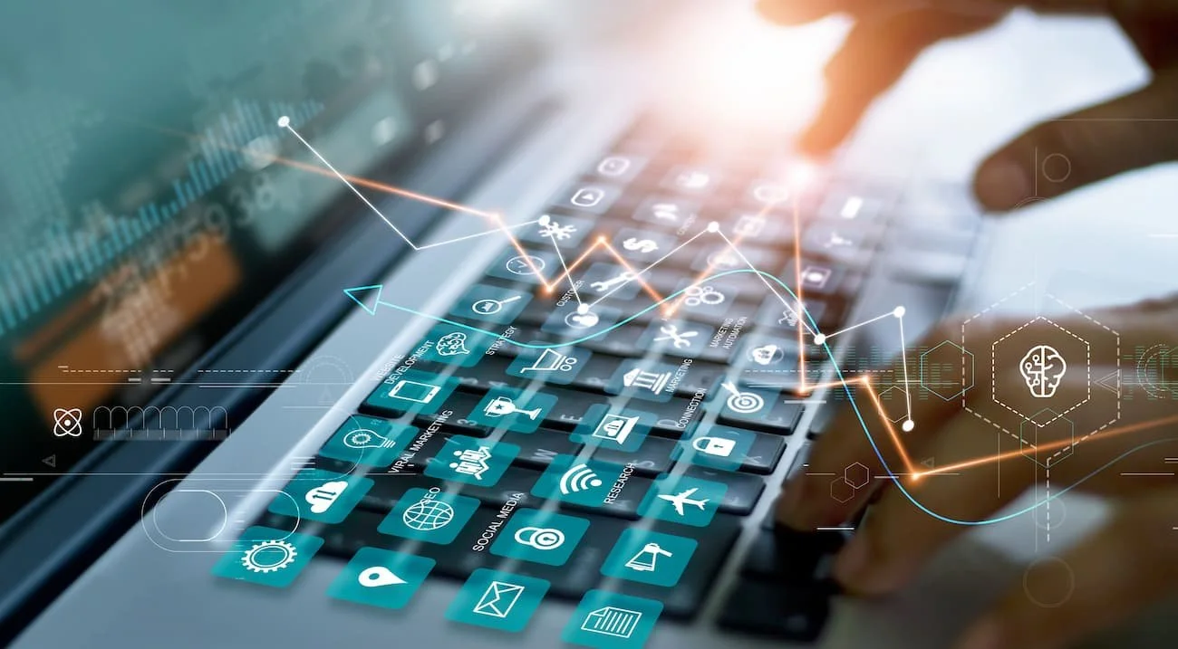 Hand tippt auf eine Tastatur eines Laptops, über der sich digitale Symbole für Technologien und soziale Medien befinden.