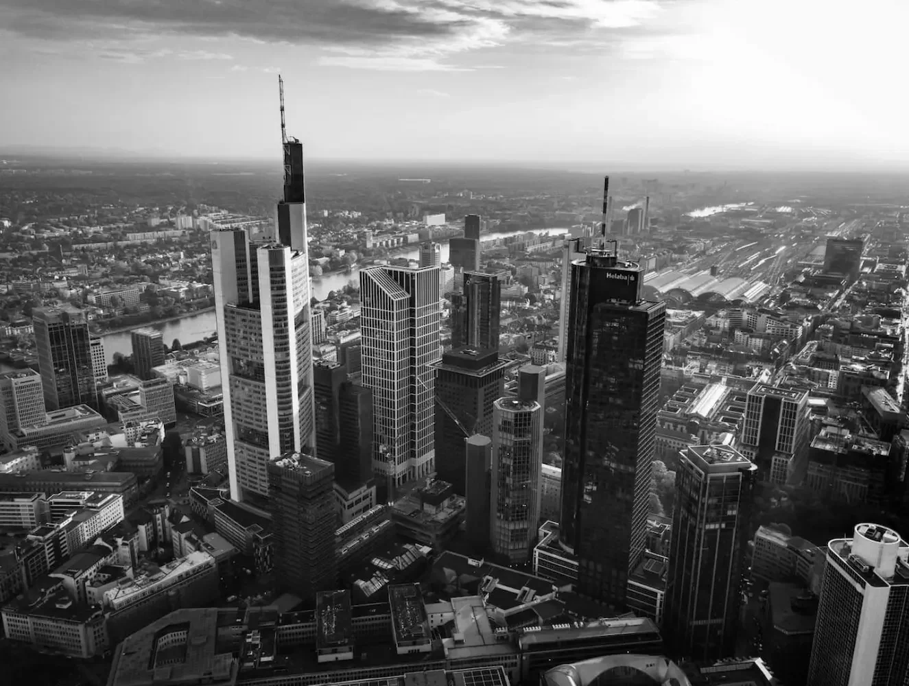 Schwarze und weiße Aufnahme einer Großstadt mit vielen Hochhäusern und einem Fluss im Hintergrund, unter einem bewölkten Himmel.