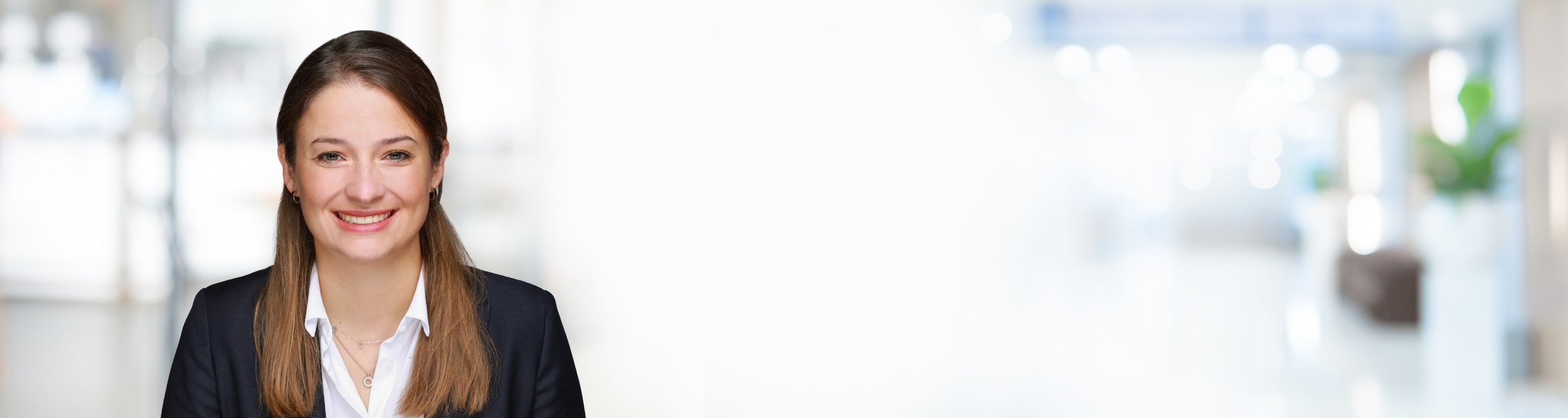 Ein Lächeln einer jungen Frau in Businesskleidung vor einem hellen, modernen Bürohintergrund.