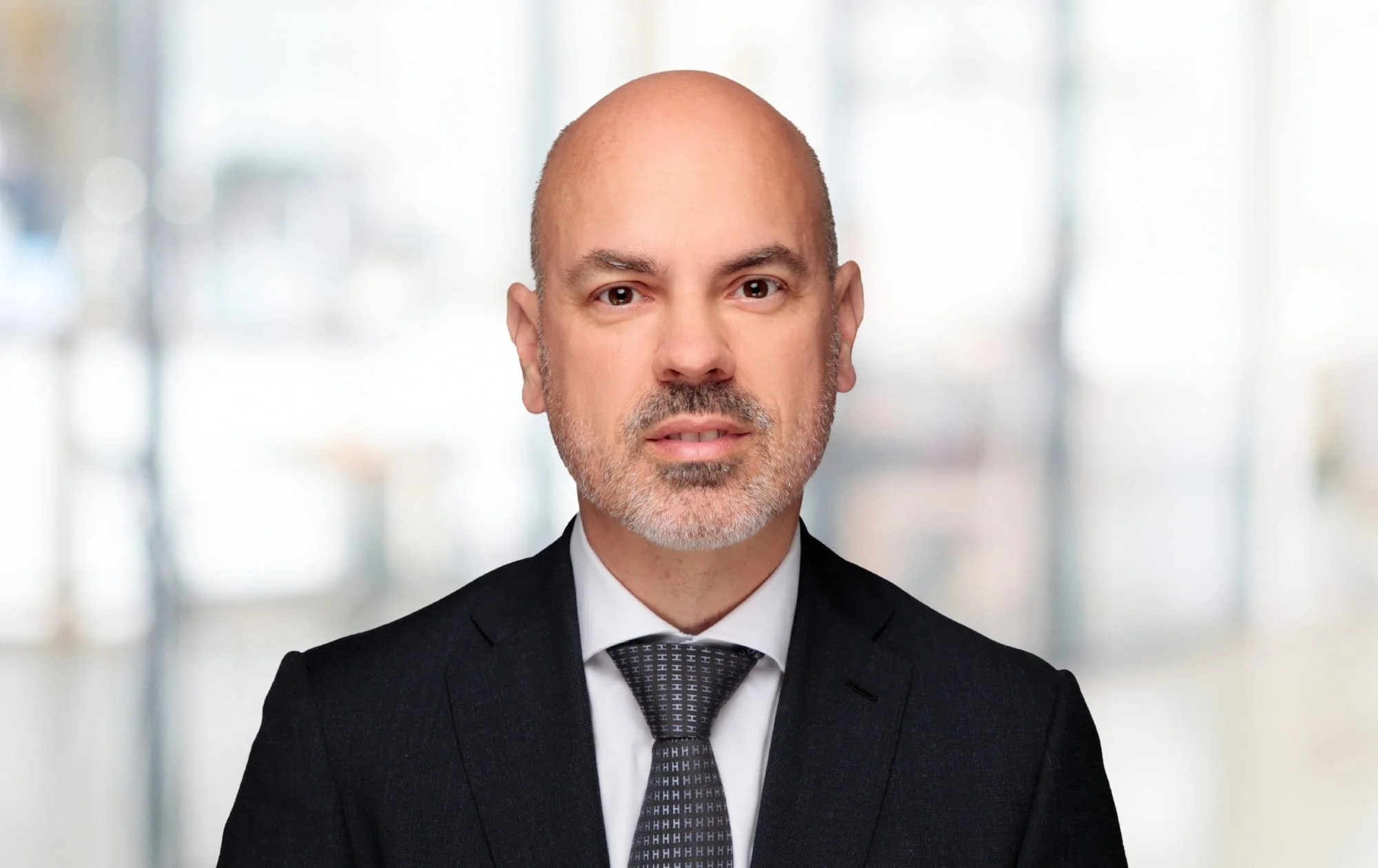 Porträt eines Mannes in Anzug vor einem unscharfen, hellen Hintergrund.