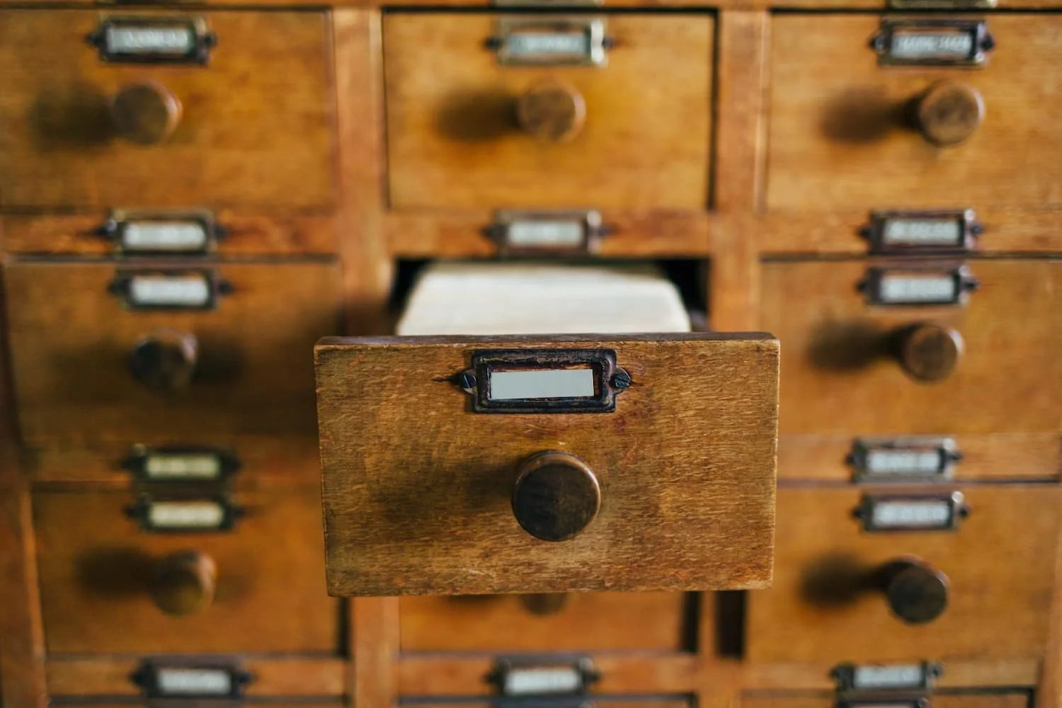 Offene Schublade eines alten Holzkastens mit mehreren kleinen Schubladen und schwarzen Griffen.