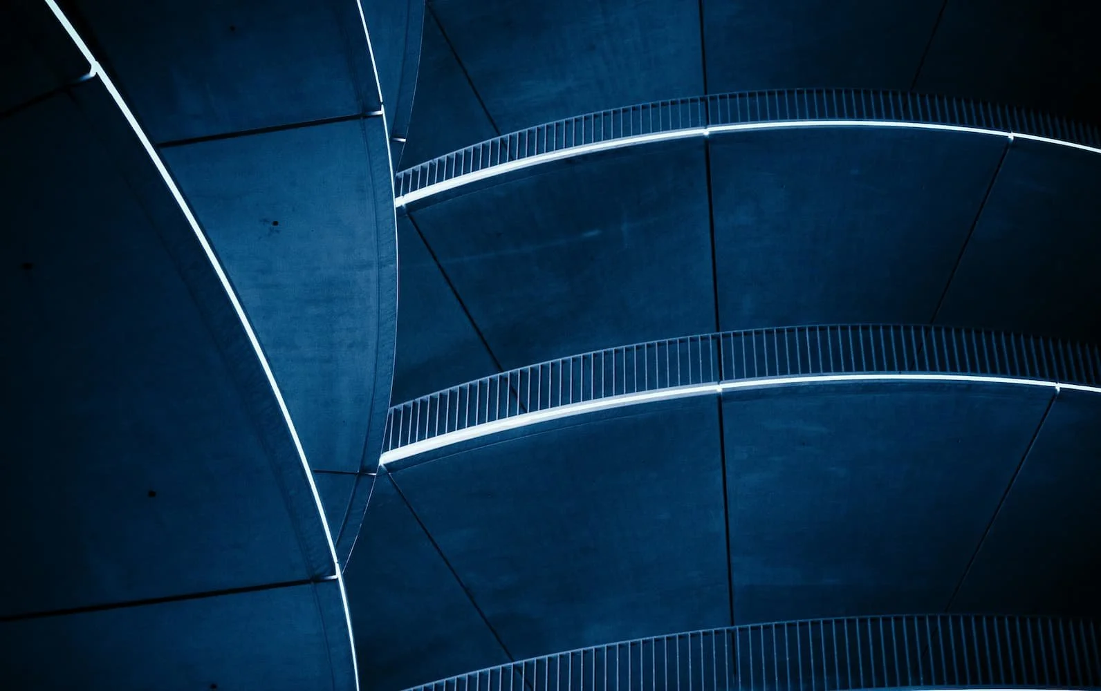 Moderne Gebäudefassade mit gebogenen, dunklen Wänden und beleuchteten Geländern auf mehreren Etagen.