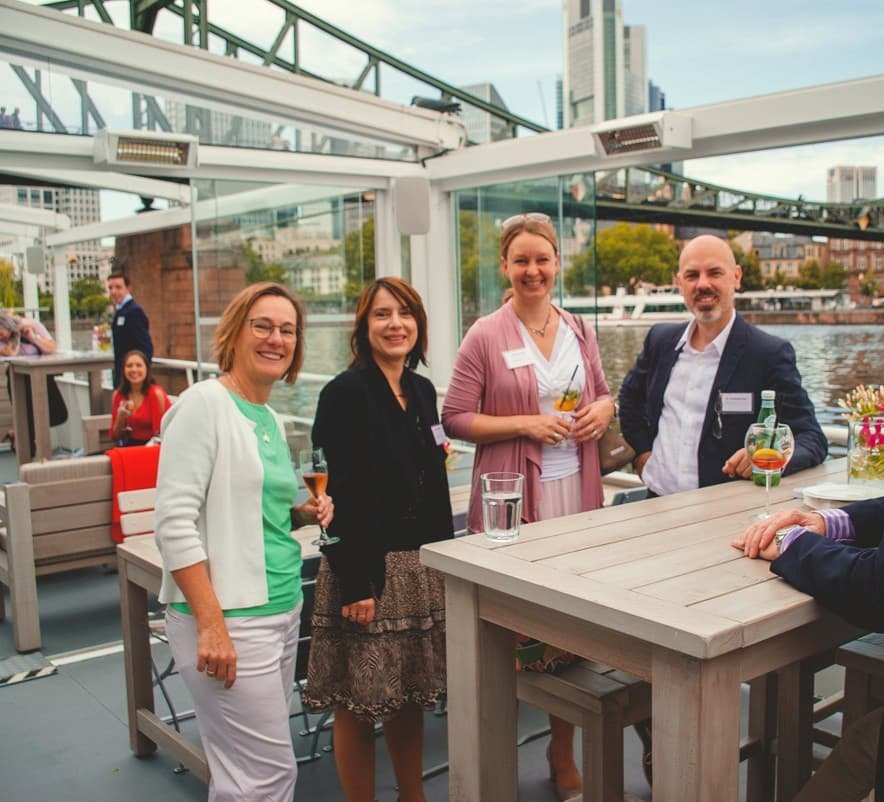 Vier Menschen auf einer Rooftop-Party mit Blick auf die Stadt, trinken cocktails und lachen.