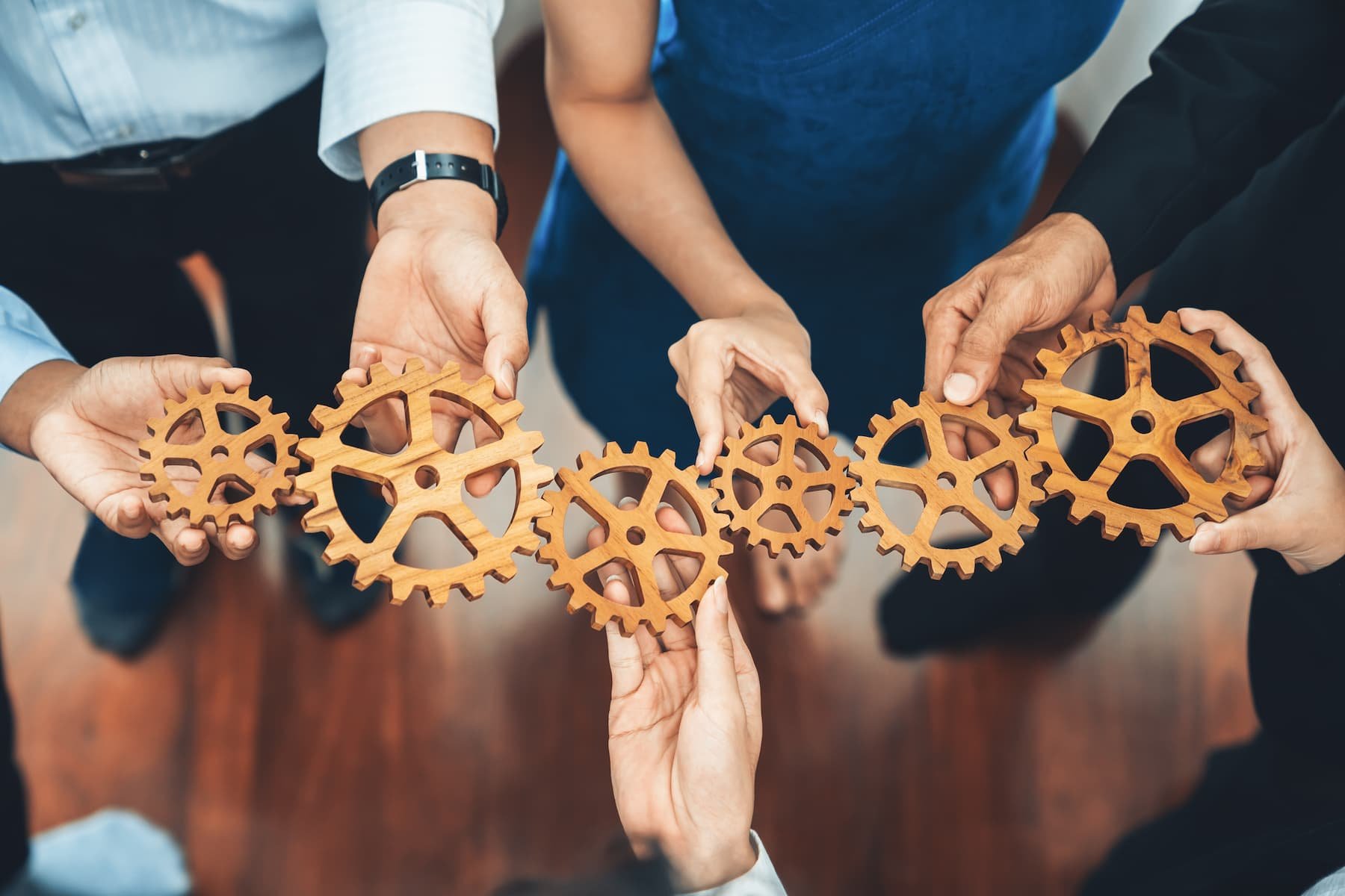 Mehrere Menschen halten zusammen eine Kette aus verbundenen Holz-Zahnrädern.