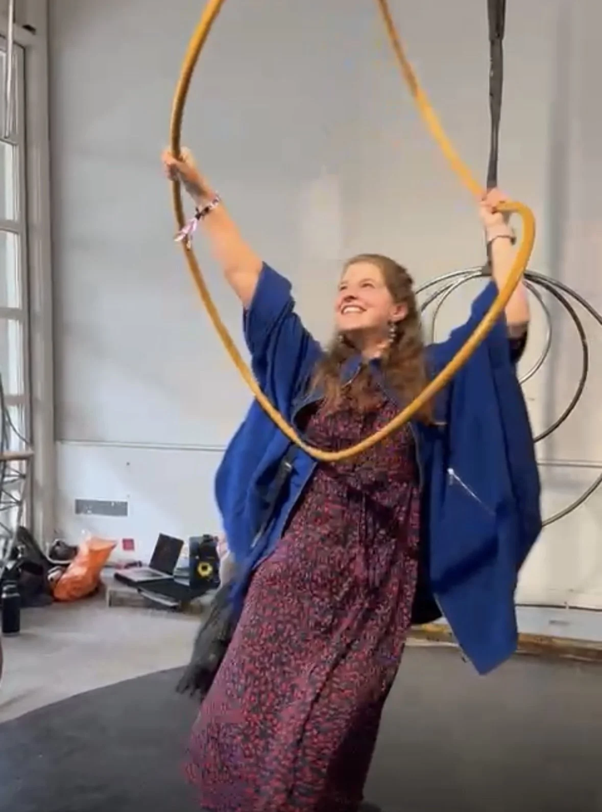 Person smiling and holding a large yellow hoop in an indoor space, surrounded by various items on the floor.