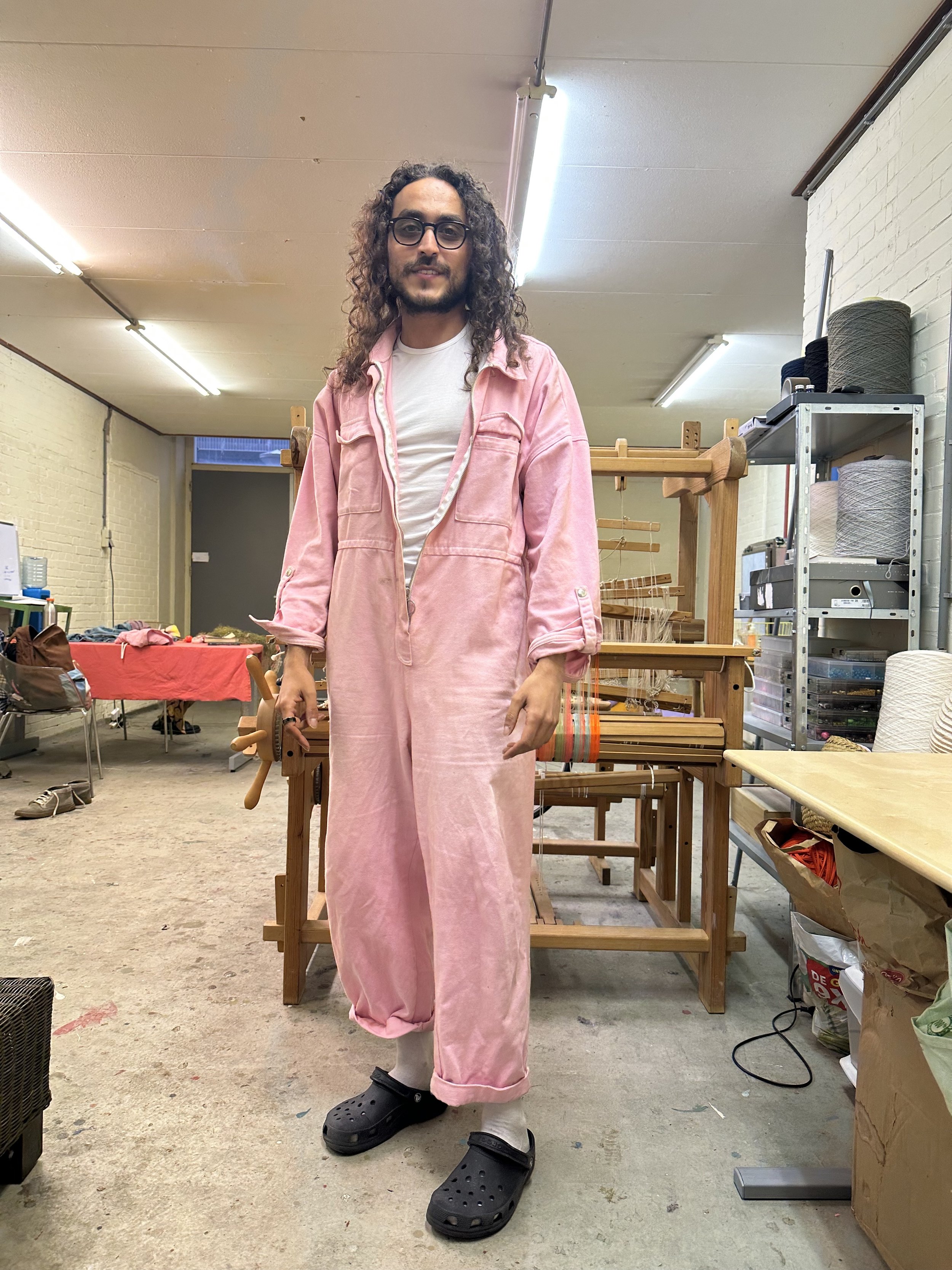 Person in a workshop wearing a pink jumpsuit and black clogs