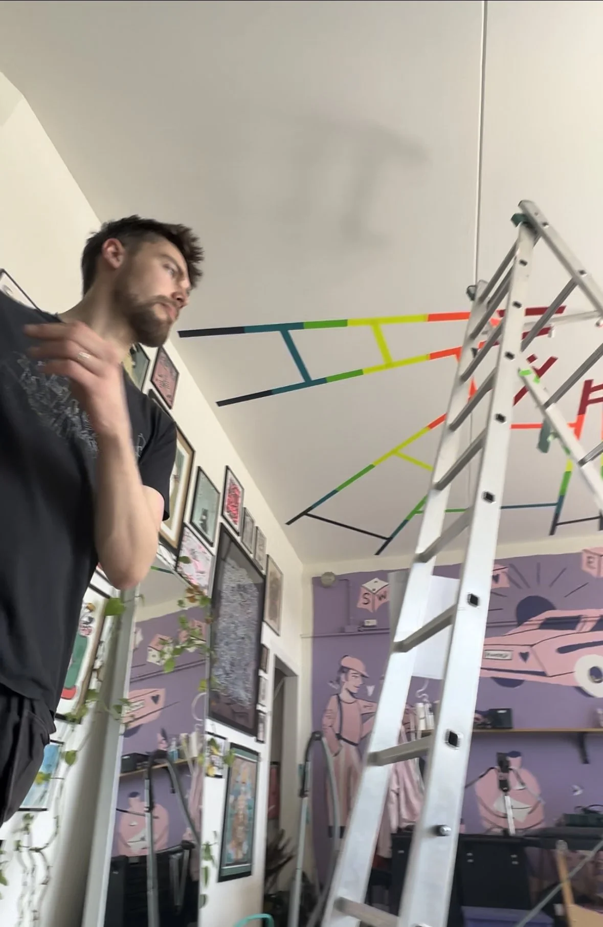 A person standing next to a ladder in a room with colorful tape designs on the ceiling and decorative wall art.