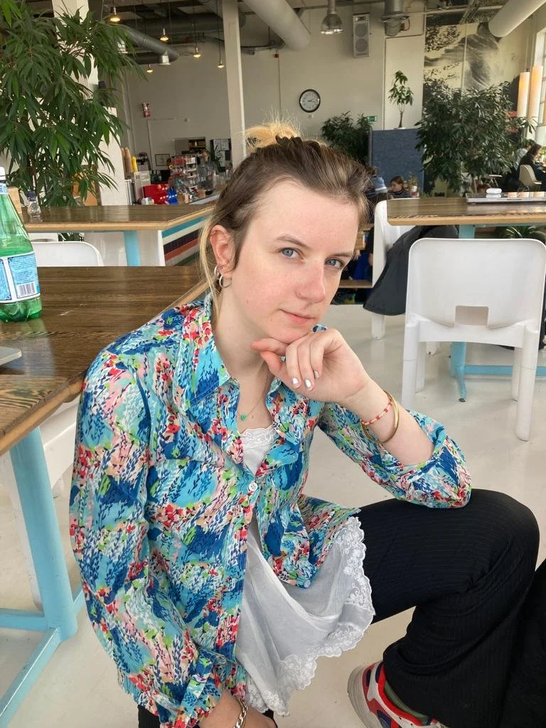 Person wearing a colorful floral shirt seated in a cafe with plants and modern decor in the background.