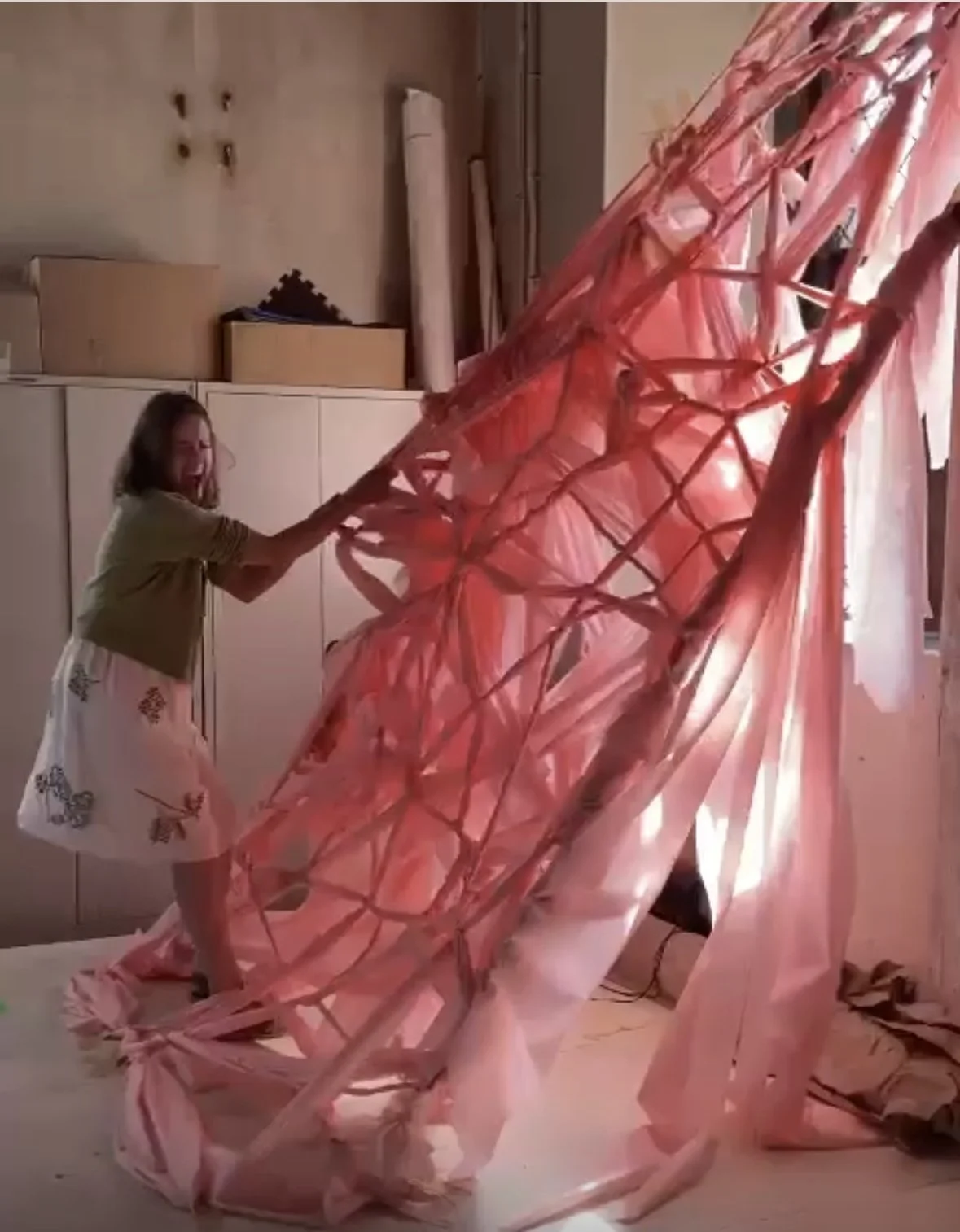 Person interacting with a large pink fabric art installation in a room with storage cabinets and various materials.