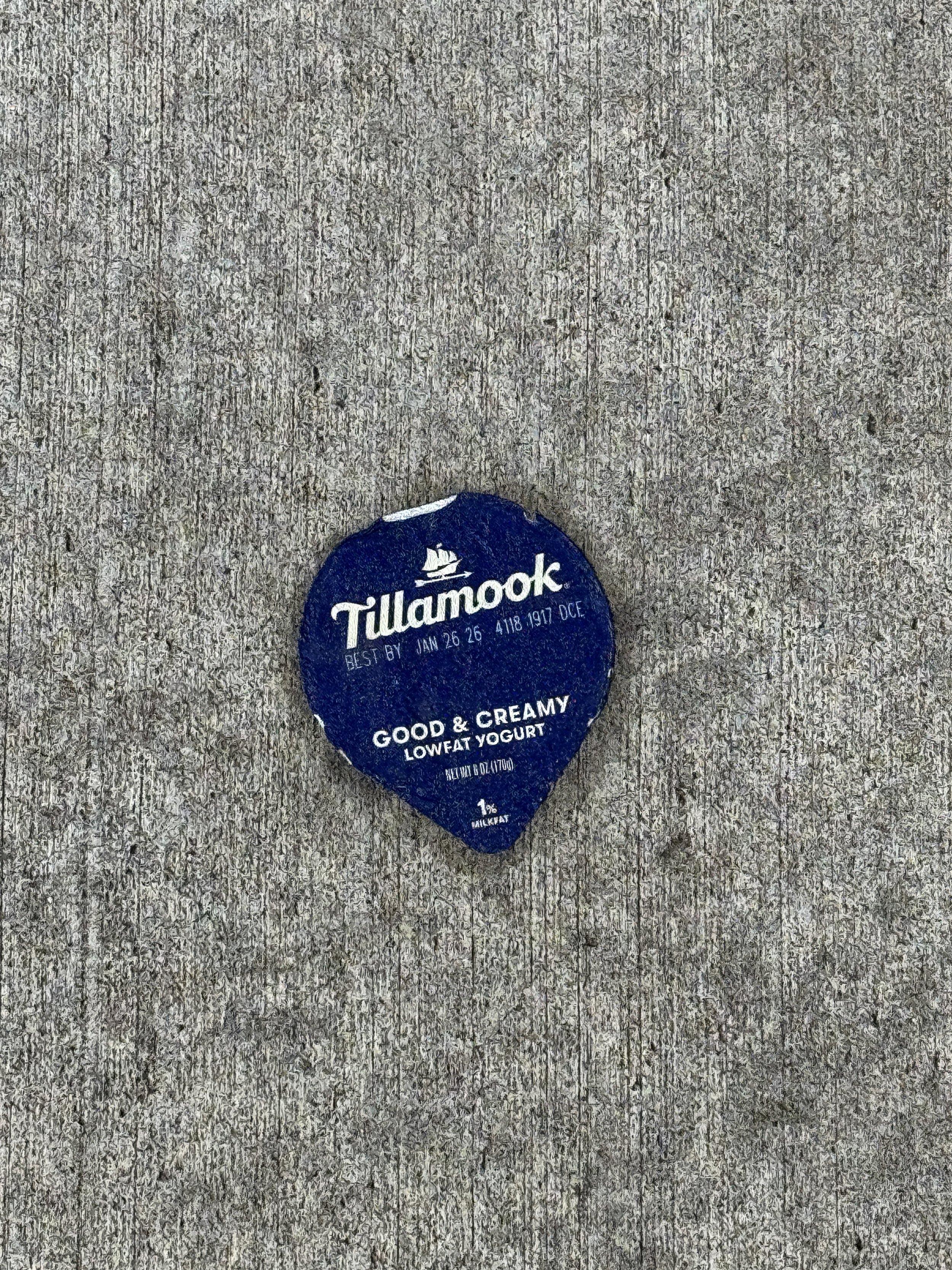 A single serving container of Tillamook low-fat yogurt with a blue lid, placed on a gray wooden surface.