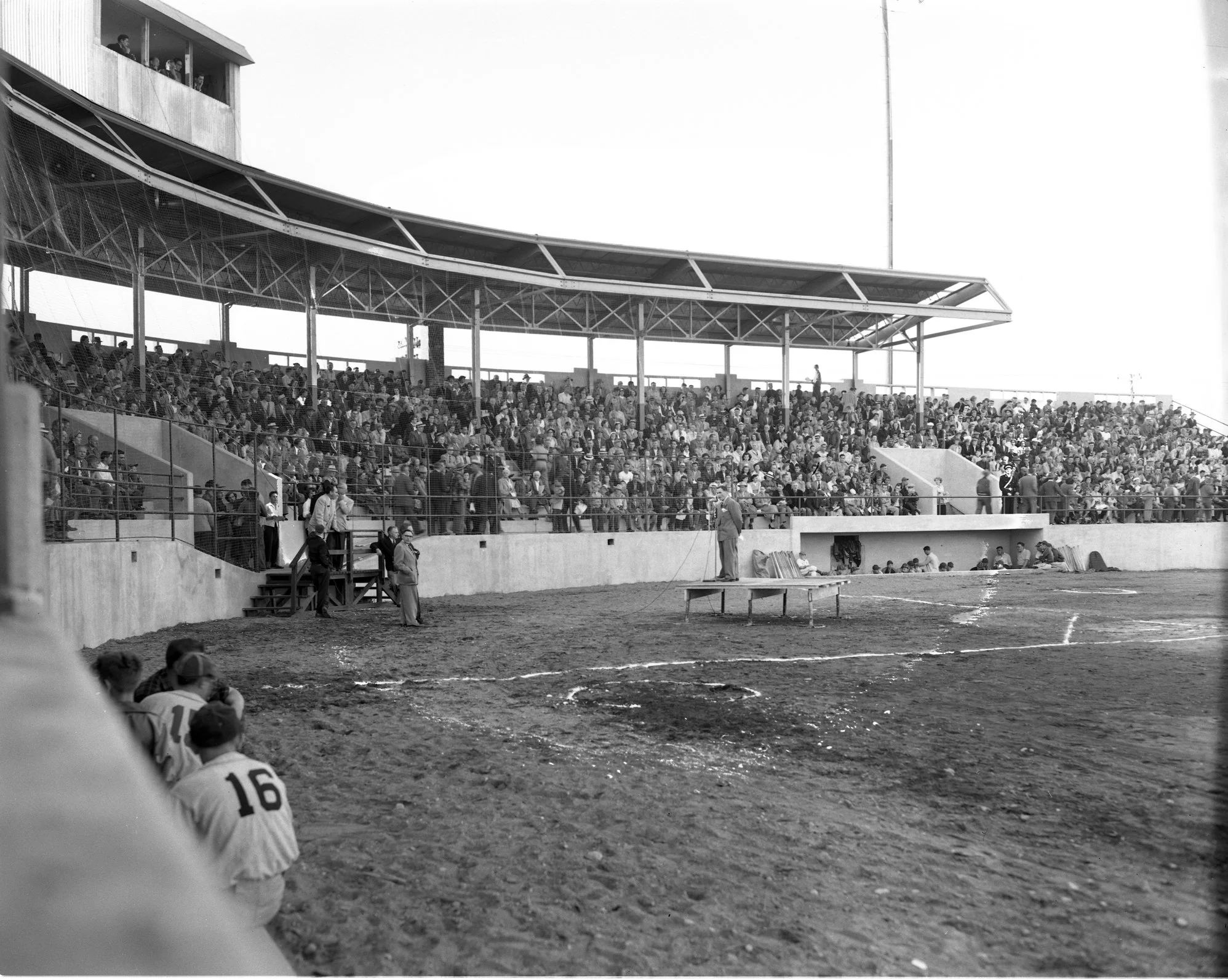 A black and white photo of someone speaking on an makeshift stage in Port Arthur Stadium with the stands full of people for the opening in 1951