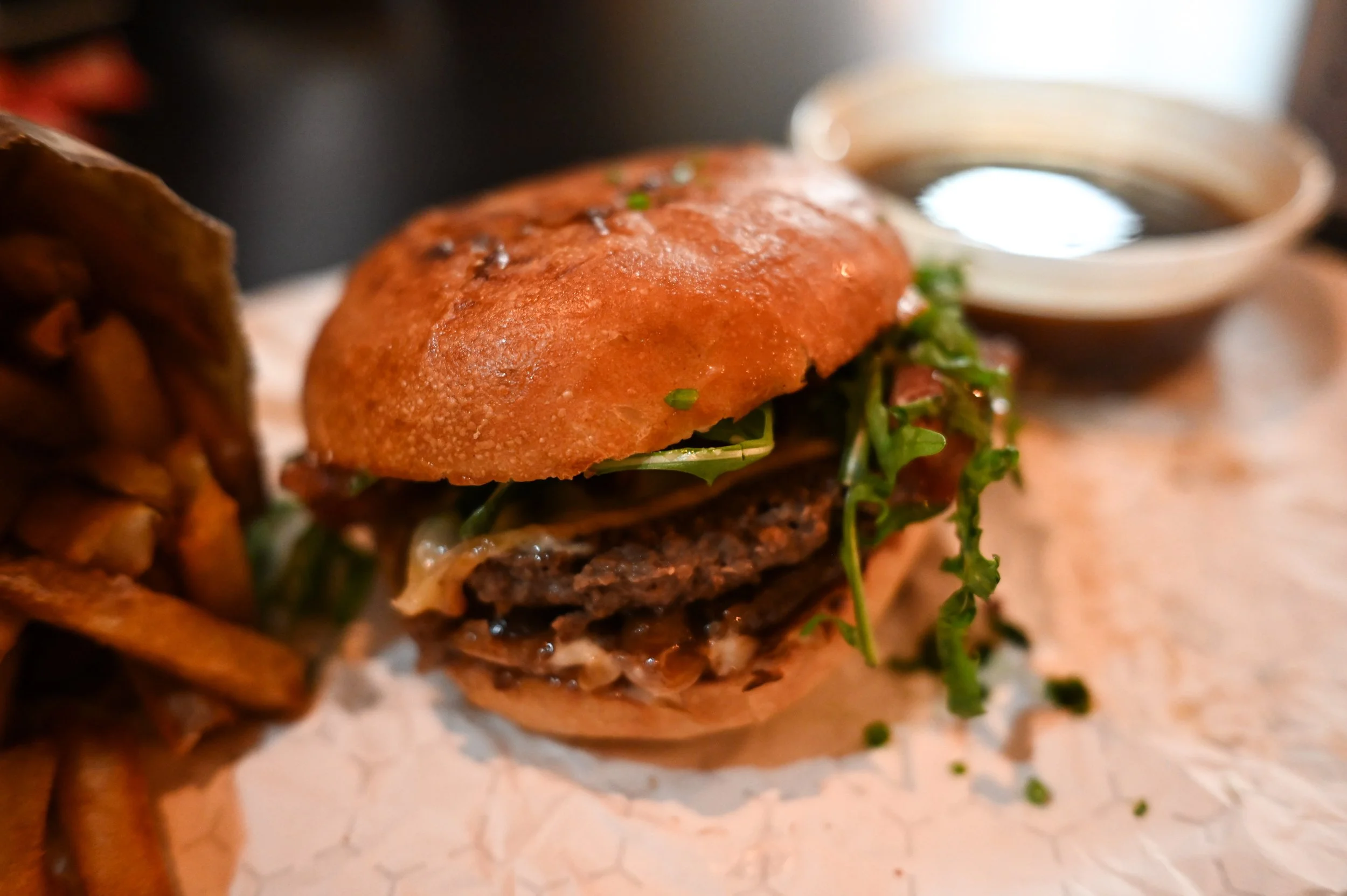 Close-up of a gourmet burger with lettuce, cheese, and a beef patty, served with a side of fries and dipping sauce.