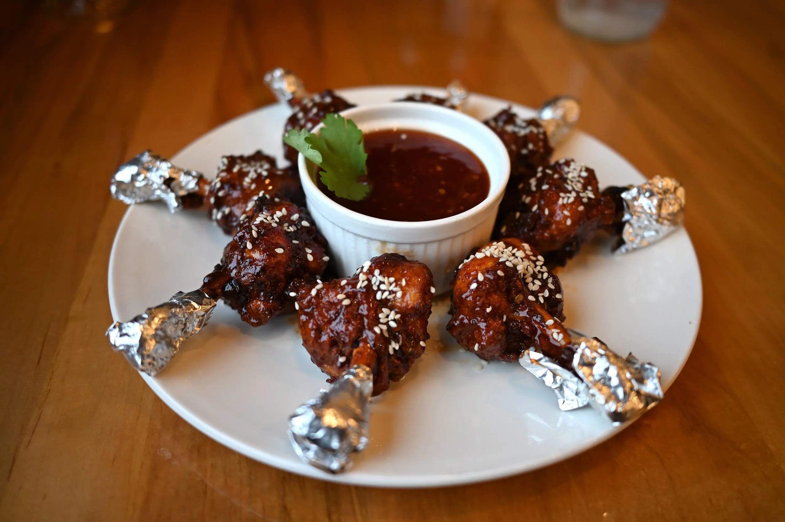 Thekkini's lollipop chicken showcasing all drumsticks on a plate surrounding a dish of sweet-and-spicy sauce