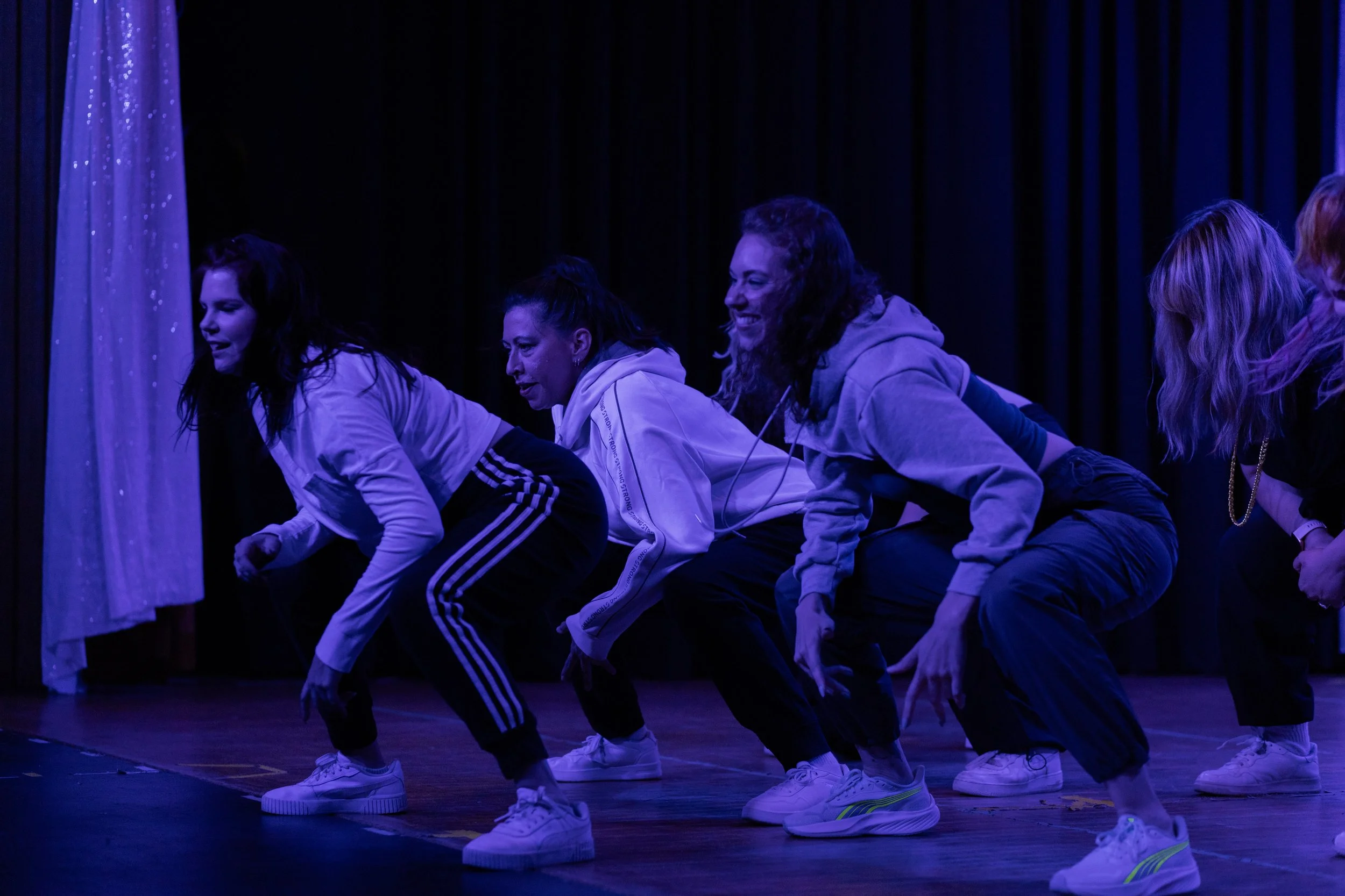 Members of Embody Dance Collective on stage performing a group number under purple stage lights