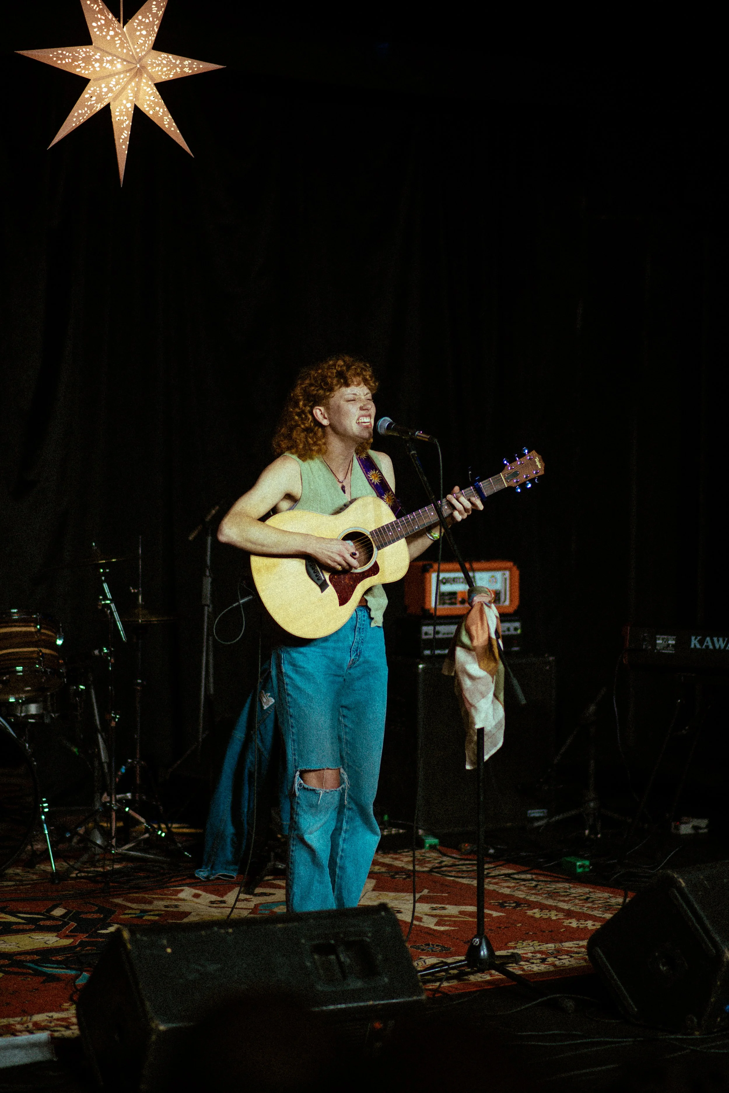 Indie folk-pop artist Cassidy Houston behind the microphone in a cozily decorated studio performing with their acoustic guitar