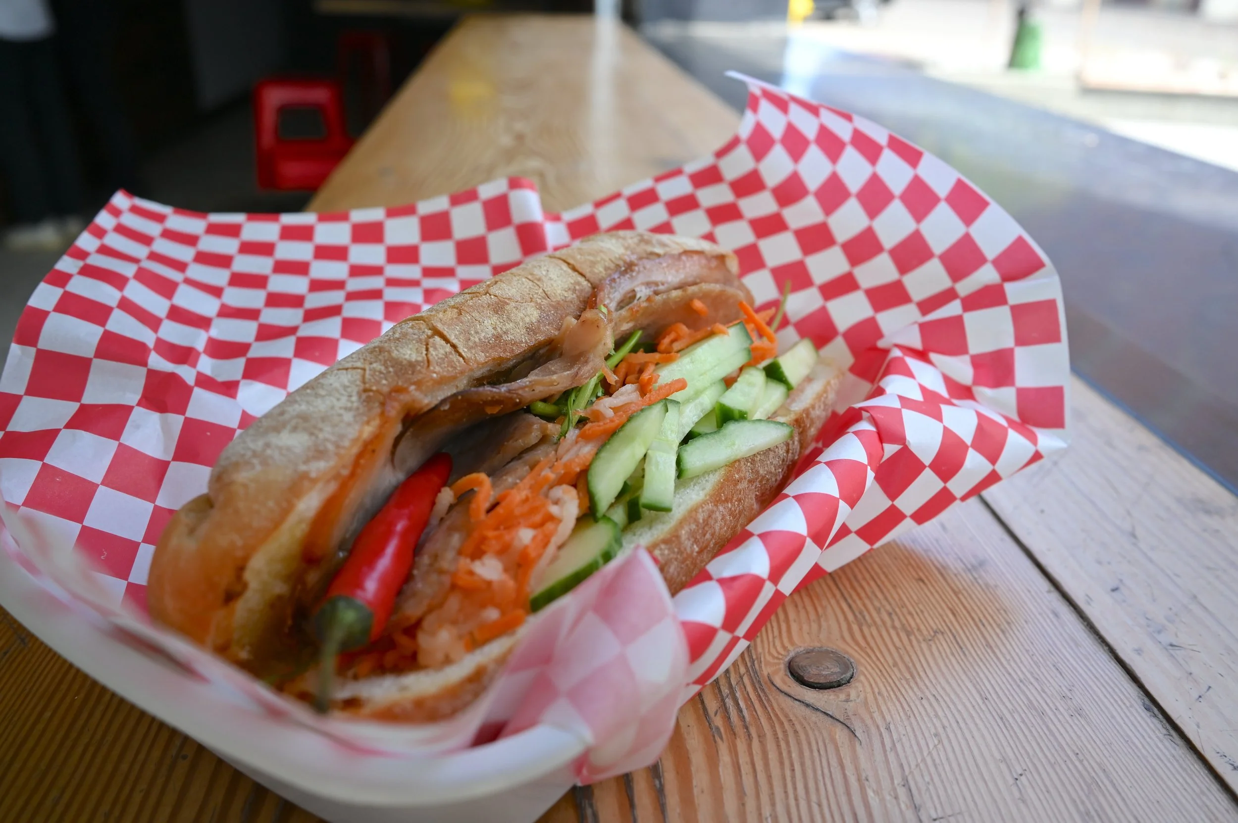Slurp It's pork banh mi sandwich on a short baguette topped with sliced cucumber, shredded carrots, pickled daikon and a red chili pepper
