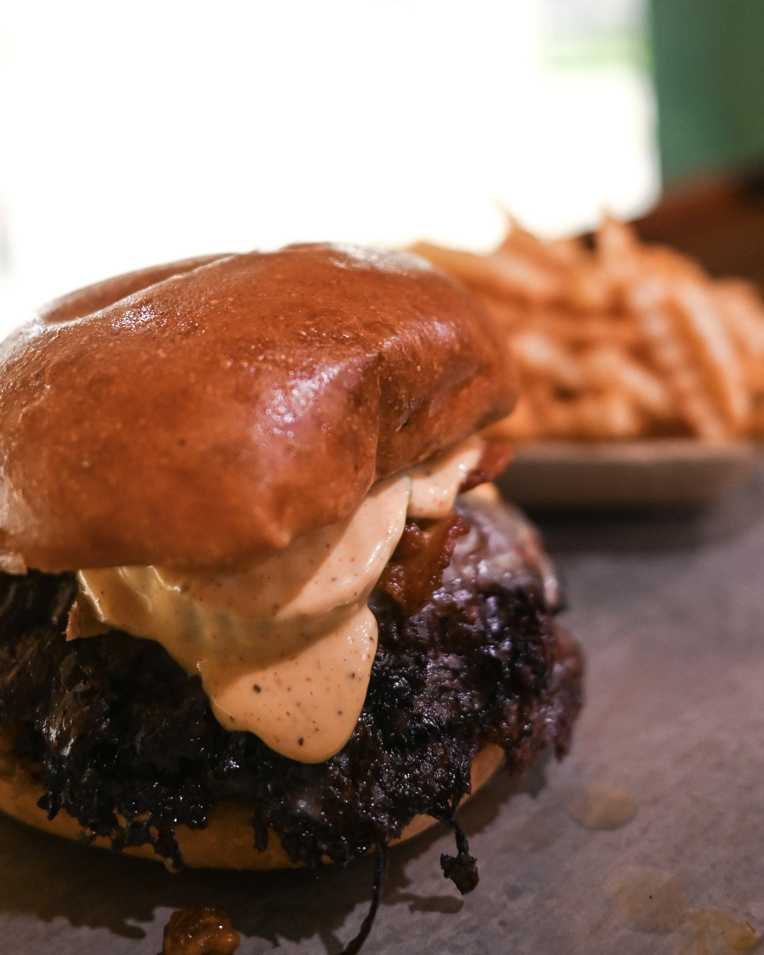 Close-up of a burger with melted cheese, crispy bacon, and a toasted bun, served with a side of French fries.