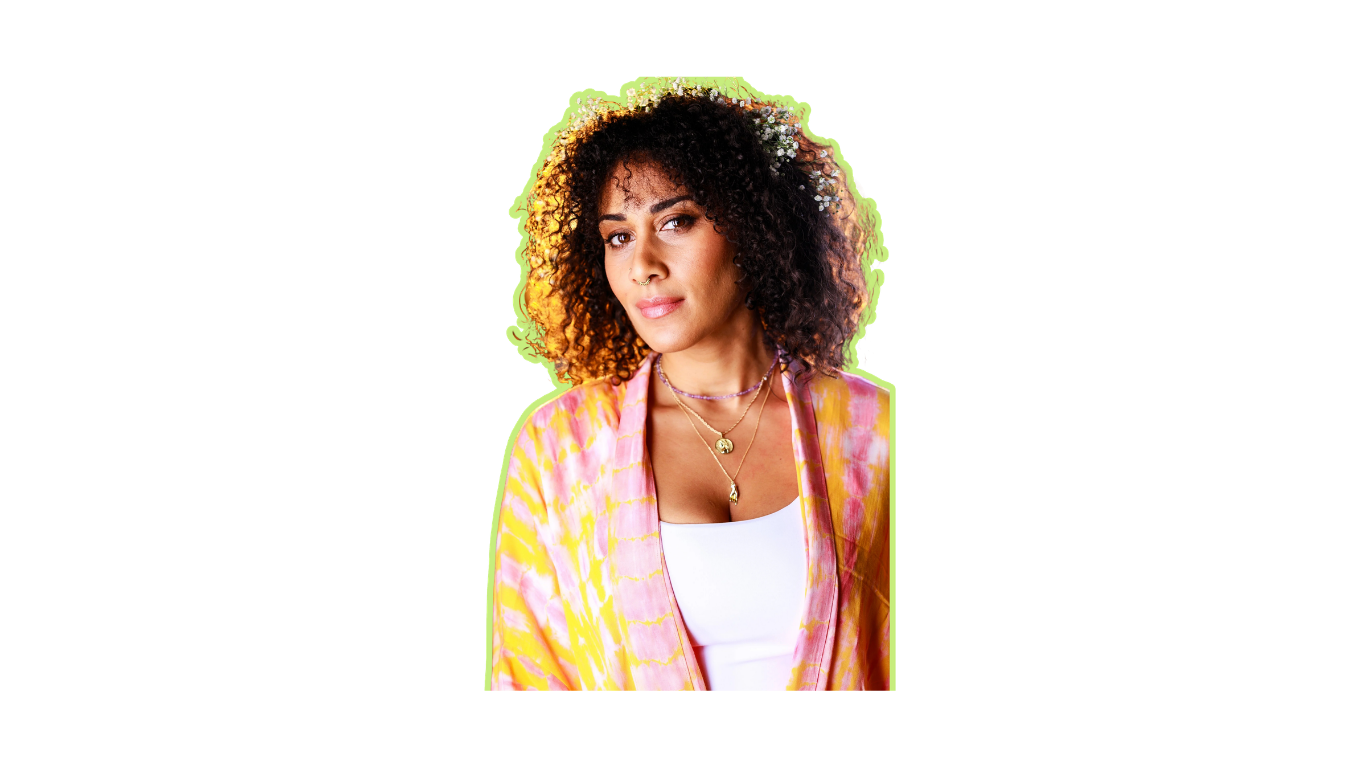 A woman with curly hair, wearing a white top and a colorful, tie-dye patterned yellow and pink jacket, looking at the camera with a slight smile.