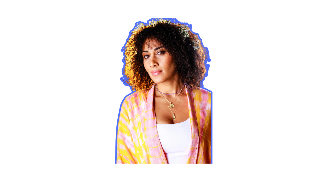 Person with curly hair and flower crown, wearing a floral shirt and layered necklaces.