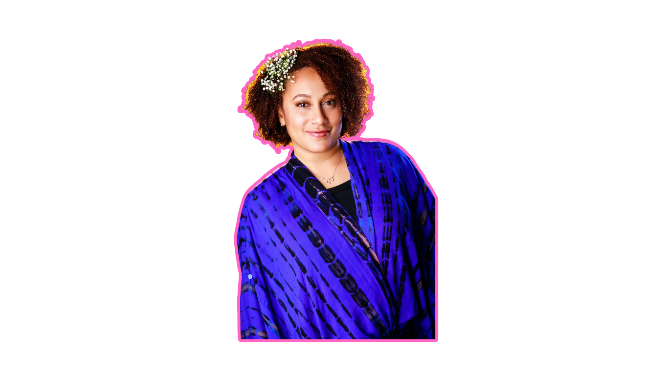Portrait of a woman with curly hair wearing a blue patterned blazer and a necklace, adorned with white flowers in her hair, smiling at the camera.