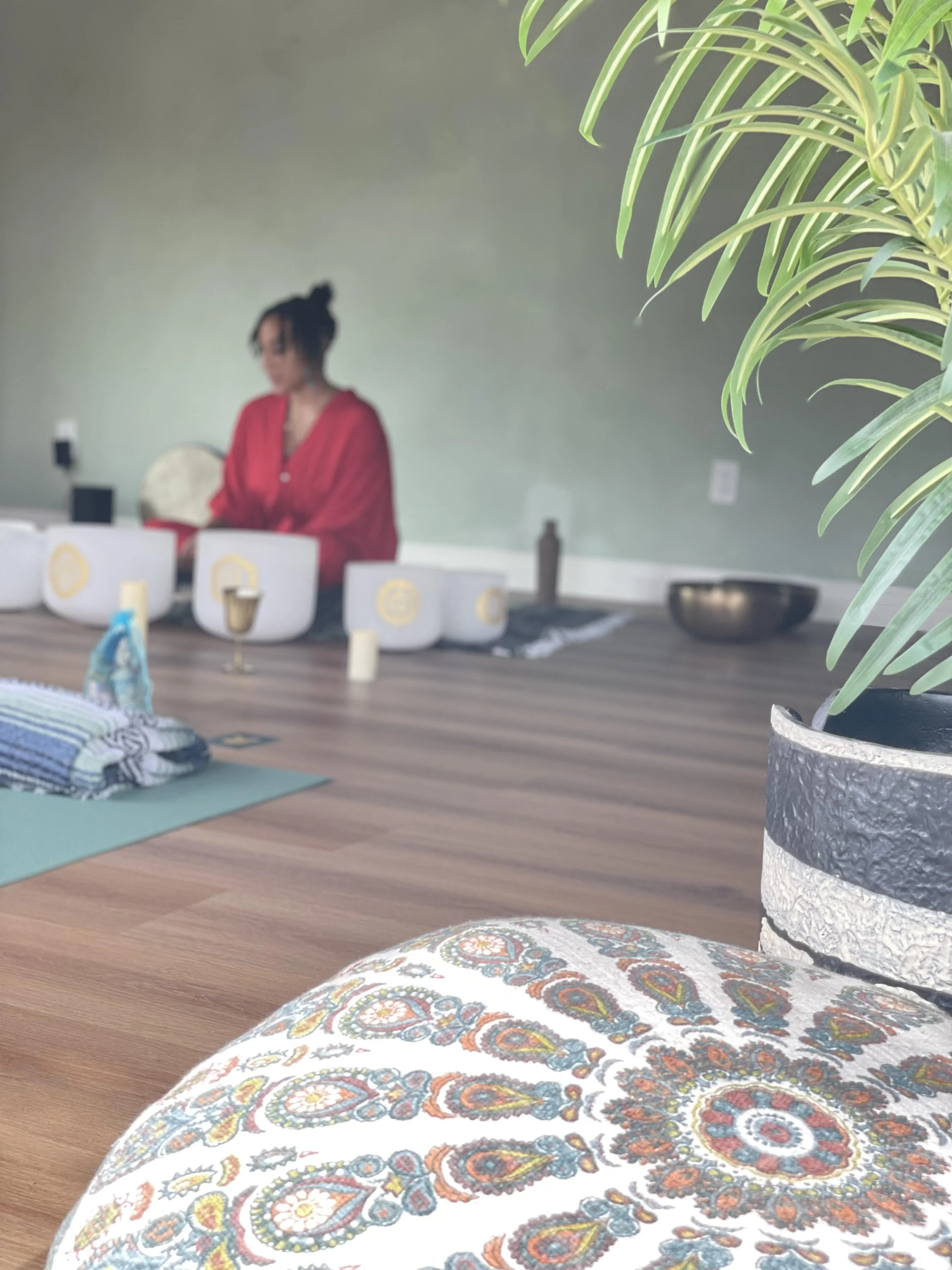 A woman meditating with singing bowls and a small hummingbird flying nearby, with a colorful, radiating background promoting summer solstice energy and sound healing.