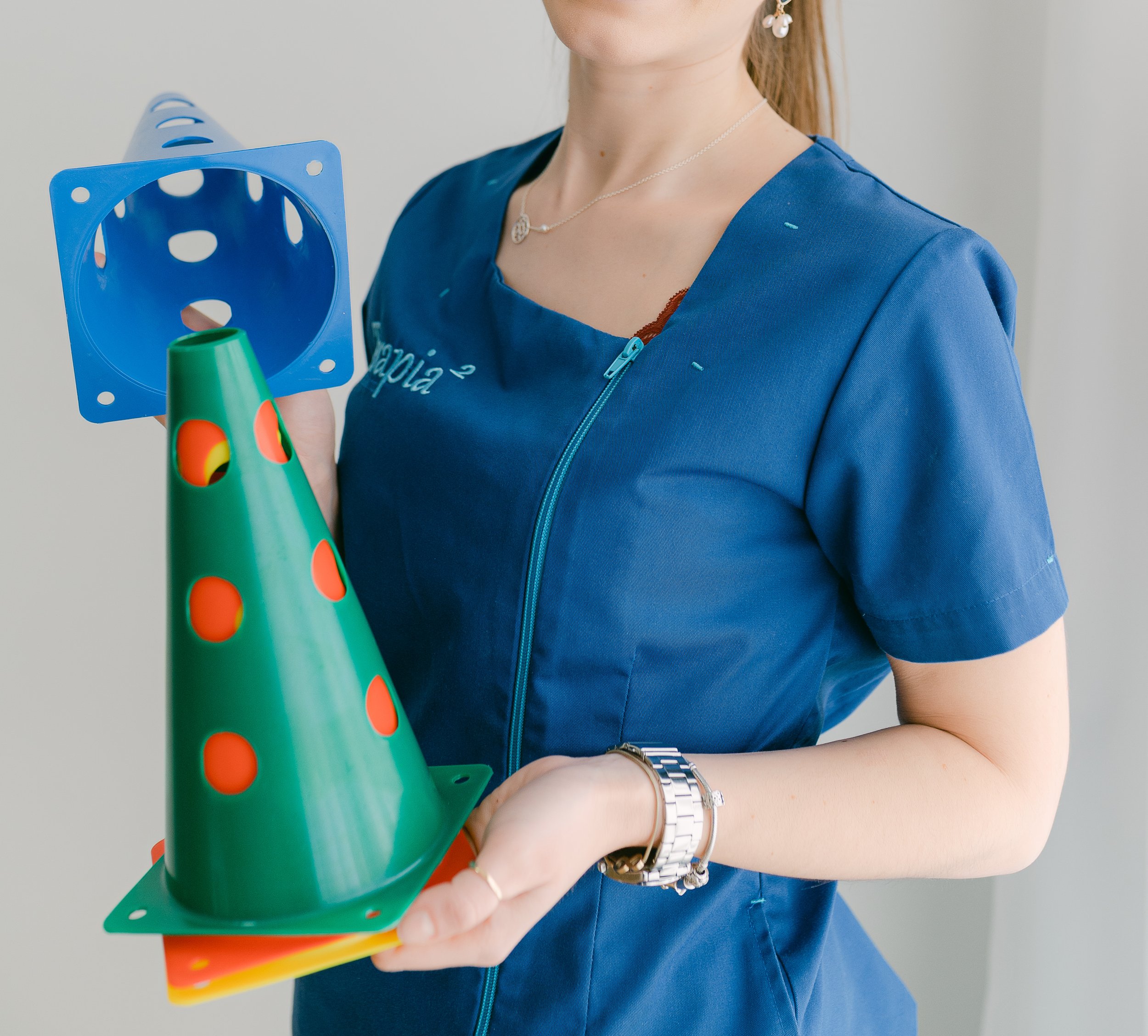 Profissional de jaleco azul segurando cones de treinamento de cores diferentes com uma estrutura de conexão.