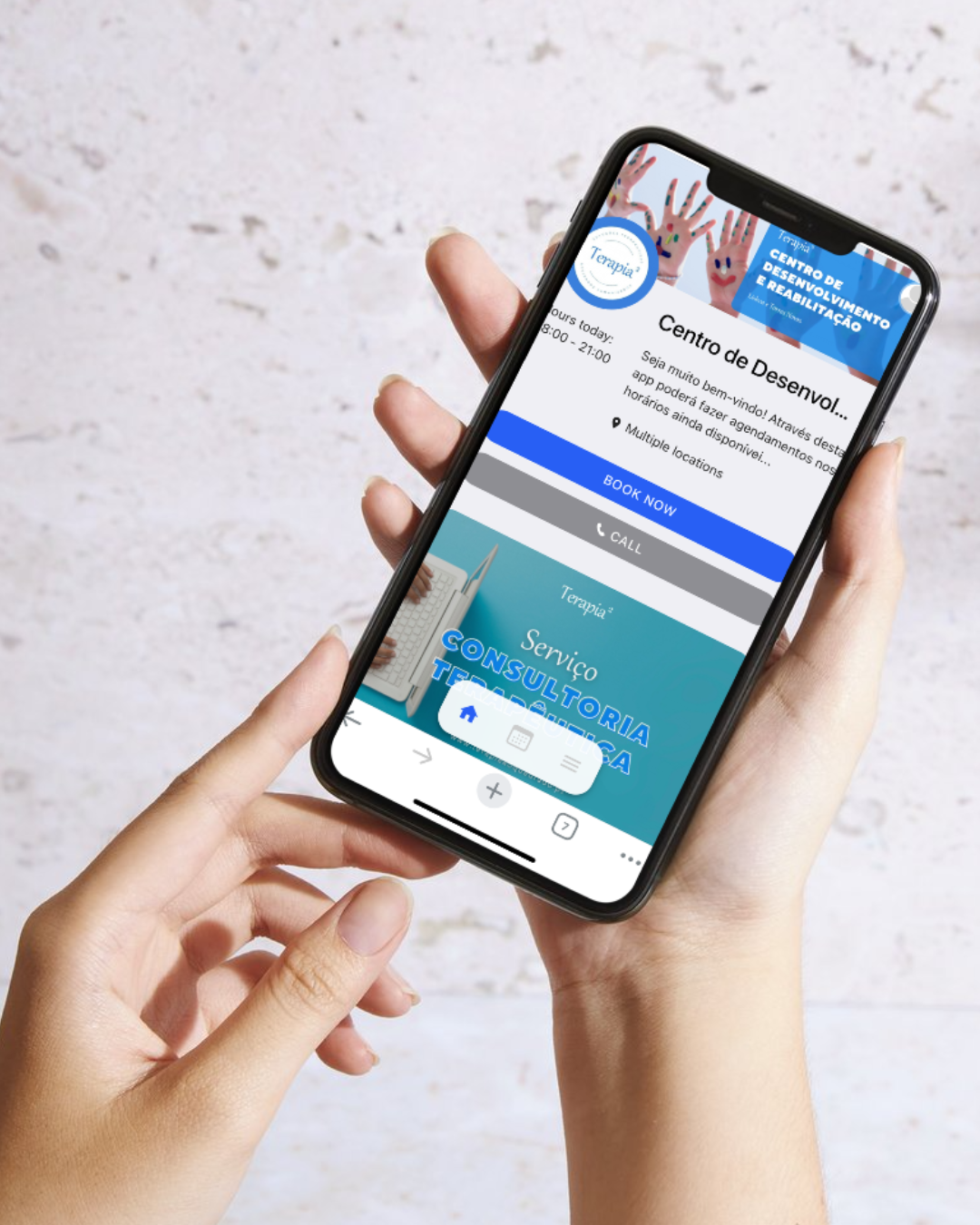 Pessoa a segurar um smartphone e exibindo o site do nosso centro de desenvolvimento e reabilitação, com destaque para o "Serviço Consultoria Terapêutica" e marcações online.