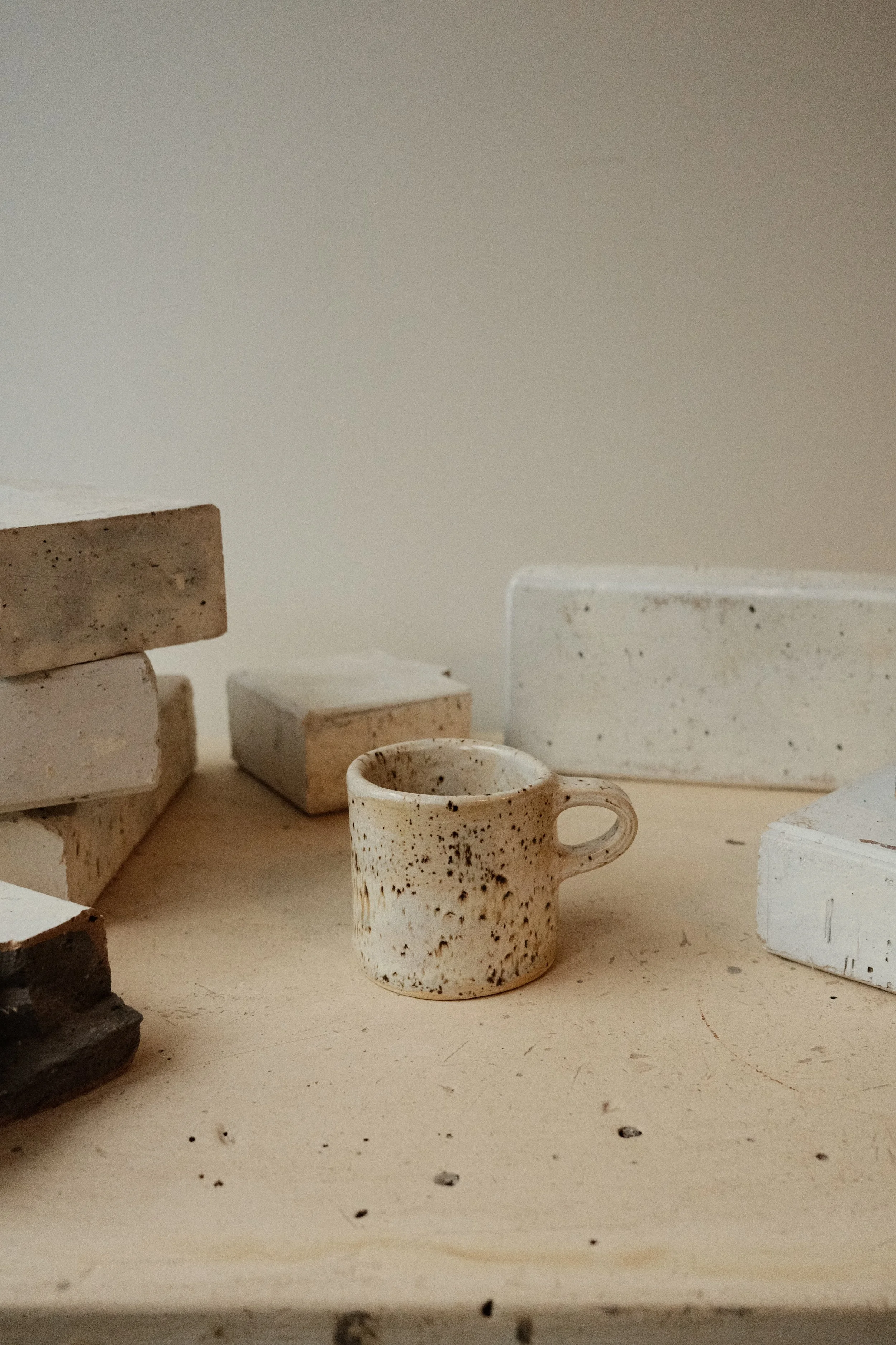 Small speckled ceramic cup surrounded by white and beige bricks on a wooden surface.