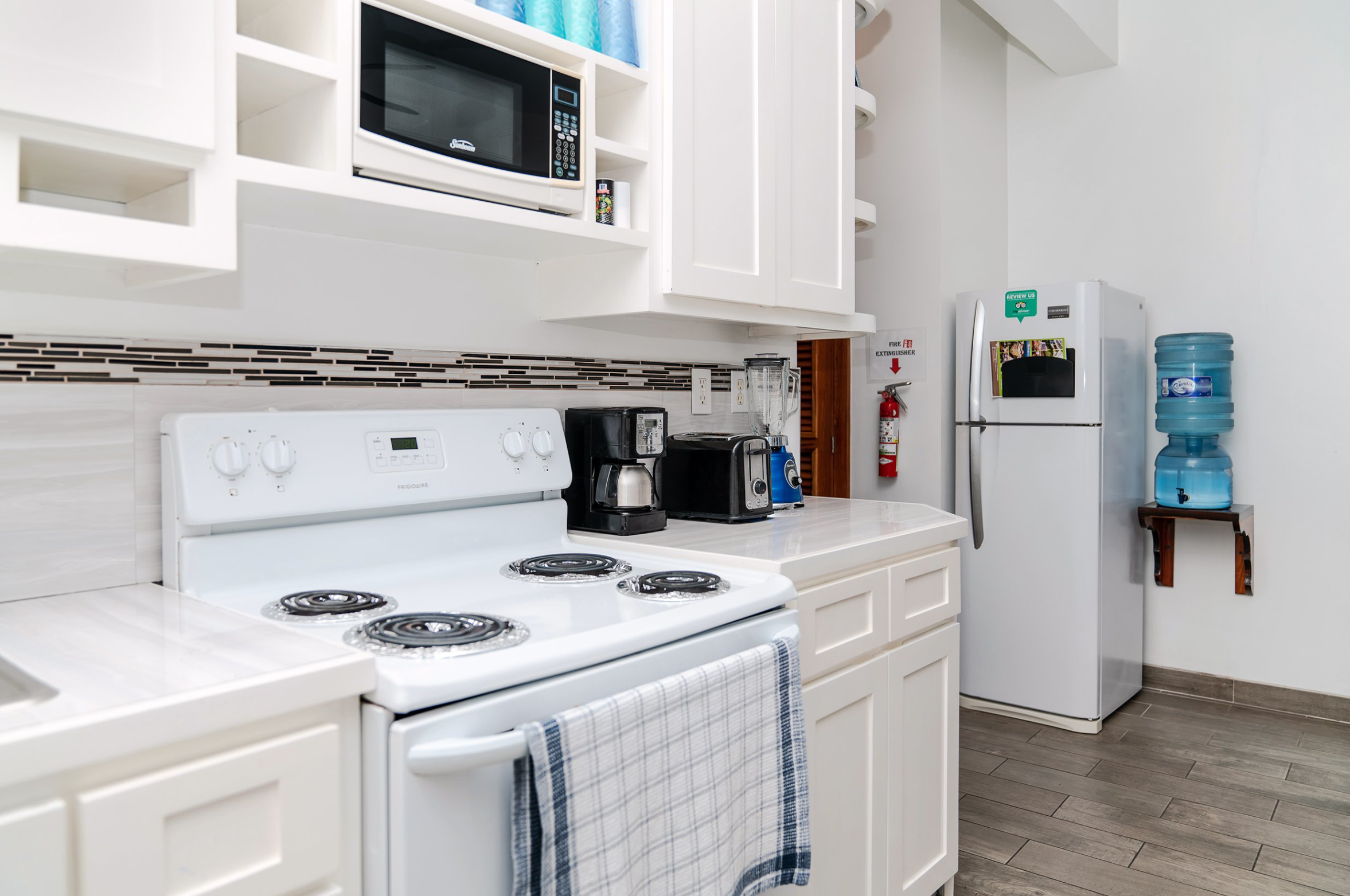 Bright kitchen with white cabinets, stove, microwave, coffee maker, toaster, blender, refrigerator, and water cooler.