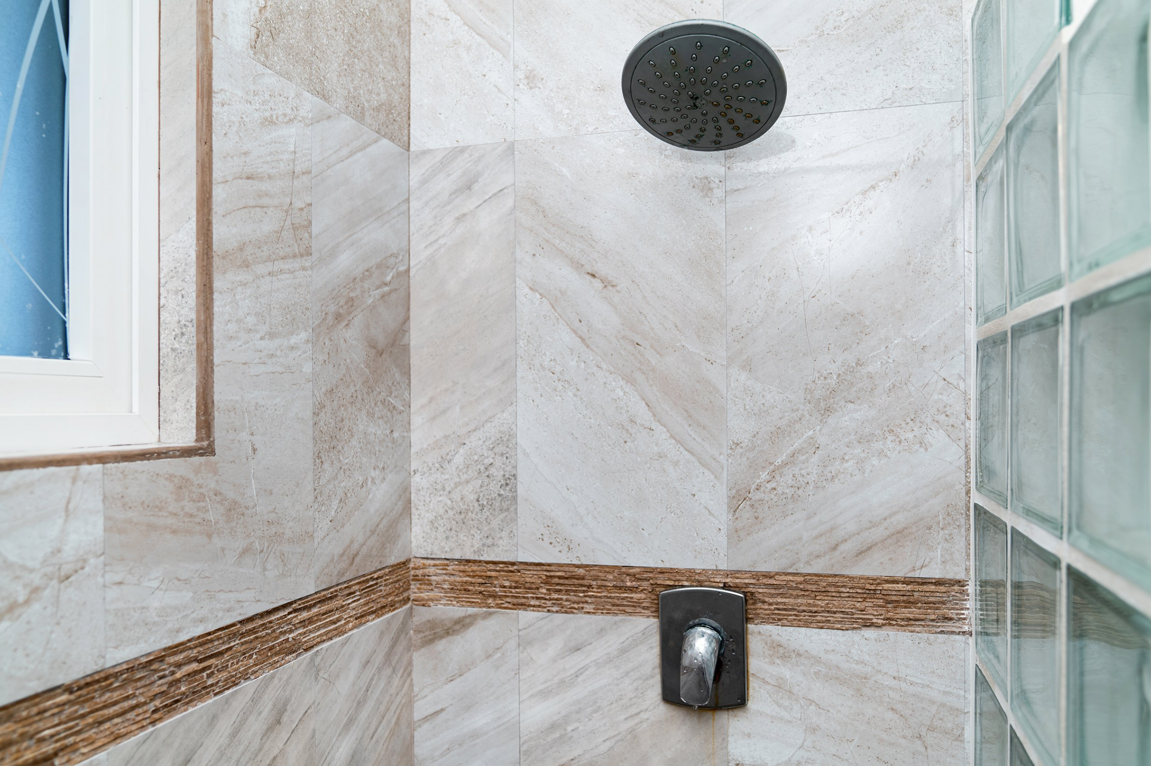 Interior of a tiled shower with a rain showerhead, glass block wall, and a window.