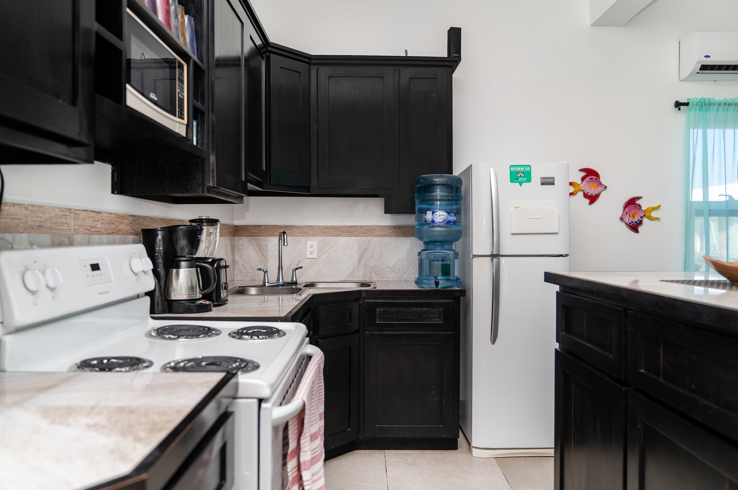 Kitchen with black cabinets, white stove, refrigerator, coffee maker, microwave, water cooler, and fish wall decorations.
