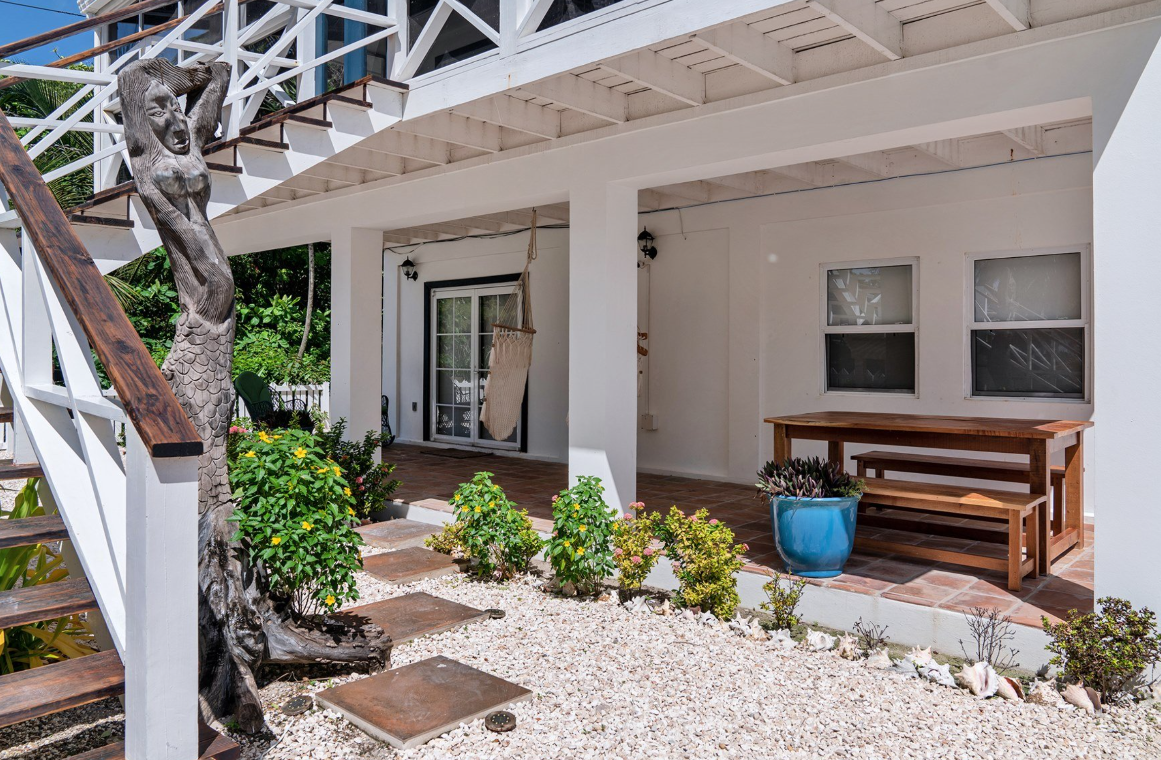 Outdoor patio with wooden mermaid sculpture, stairs, plants, and a table with benches.