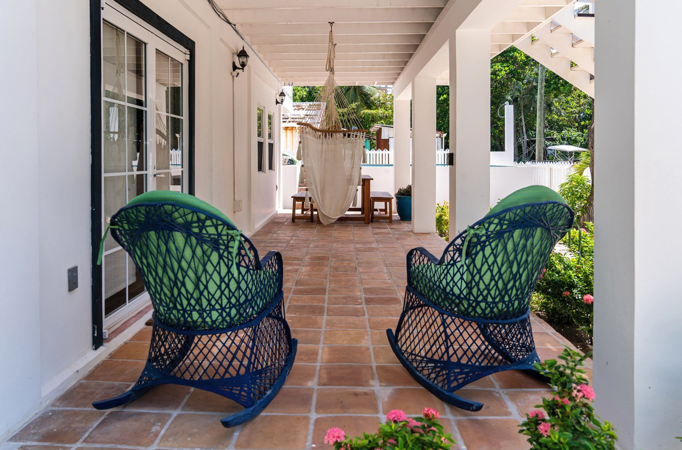 Outdoor patio with wicker rocking chairs, a hammock, terracotta floor tiles, and a table with benches. San pedro belize real estate proptery