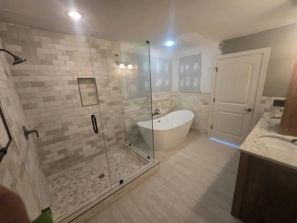 Bathroom with glass shower enclosure, freestanding bathtub, wooden vanity, and tiled walls and floor.