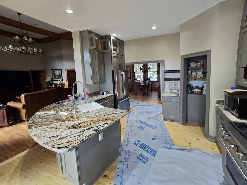 View of a kitchen with a gray island, granite countertop, stainless steel appliances, and an adjacent dining room with a wooden table and chairs.
