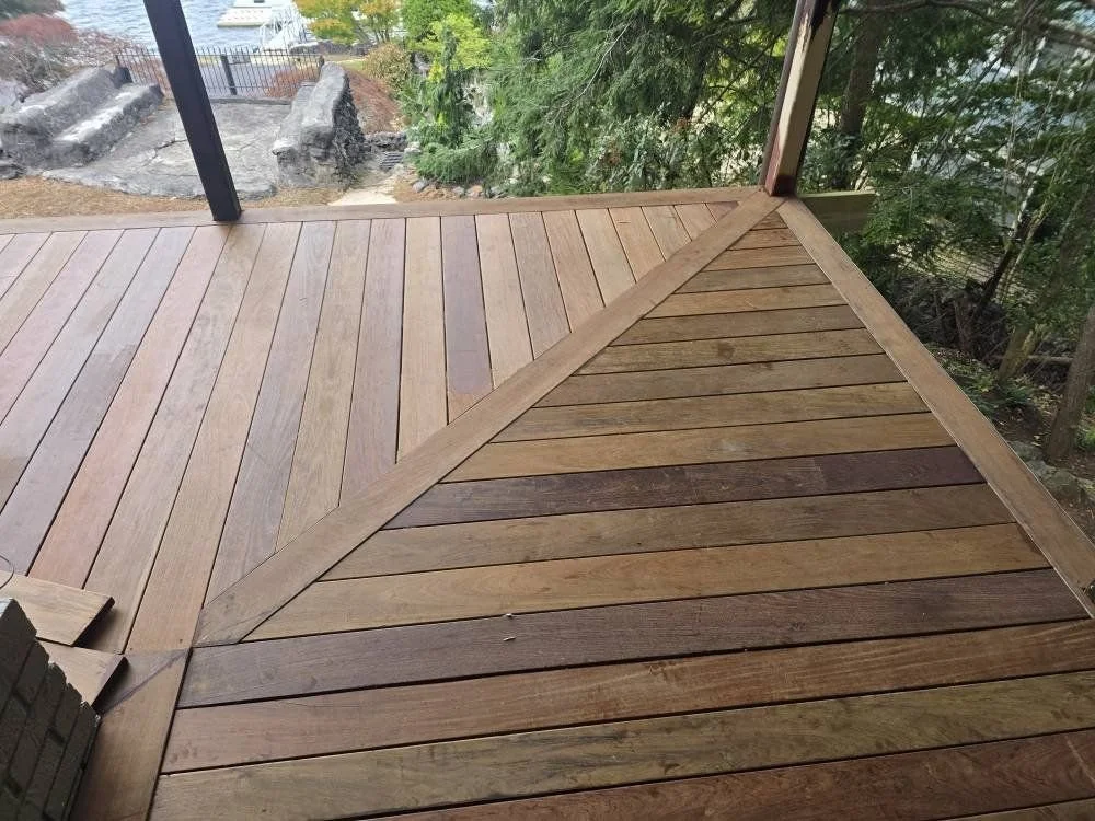 Close-up of a wooden deck with diagonal and straight plank patterns, surrounded by a natural outdoor setting with trees and plants.