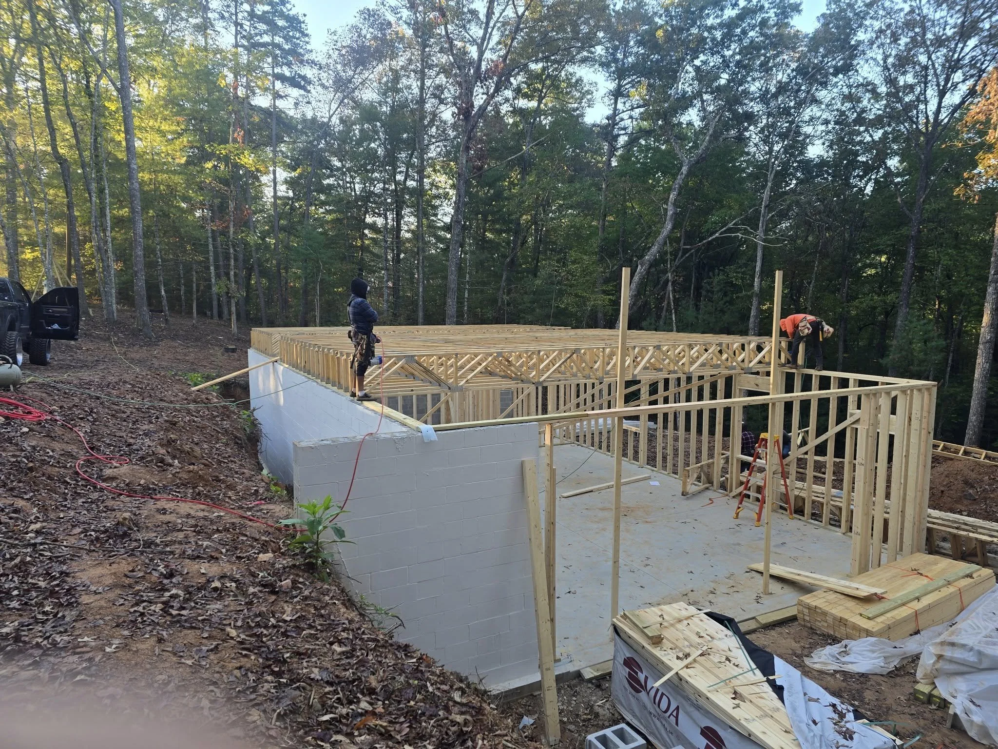 Construction workers building a wooden deck or platform on a concrete foundation, in a wooded area.