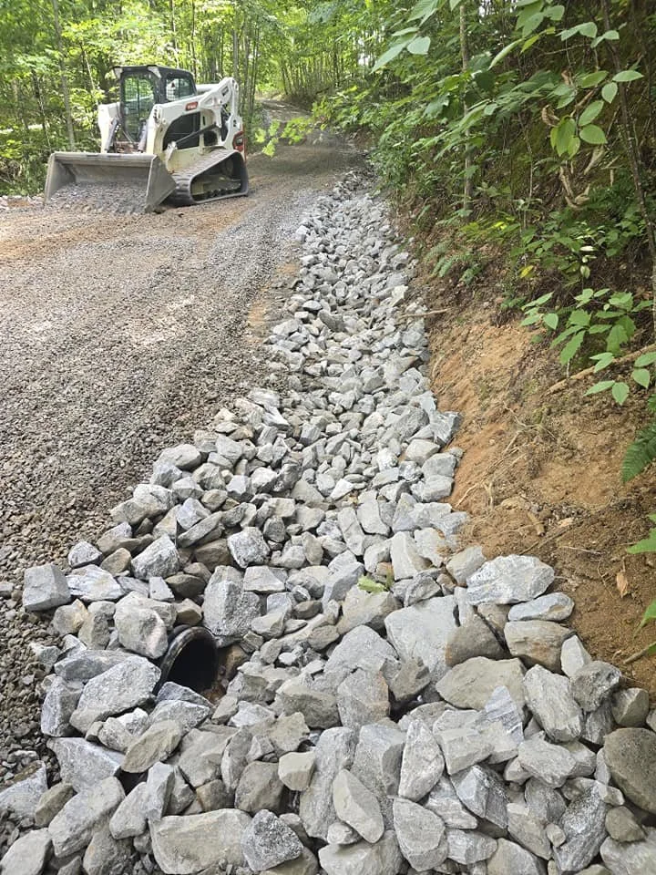 A bulldozer spreading gravel on a forested dirt road to repair or construct the road.