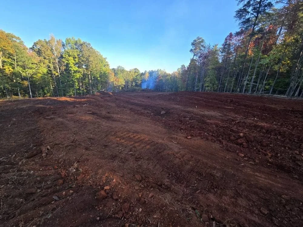 Freshly cleared and leveled land for construction with trees in the background and a clear blue sky.