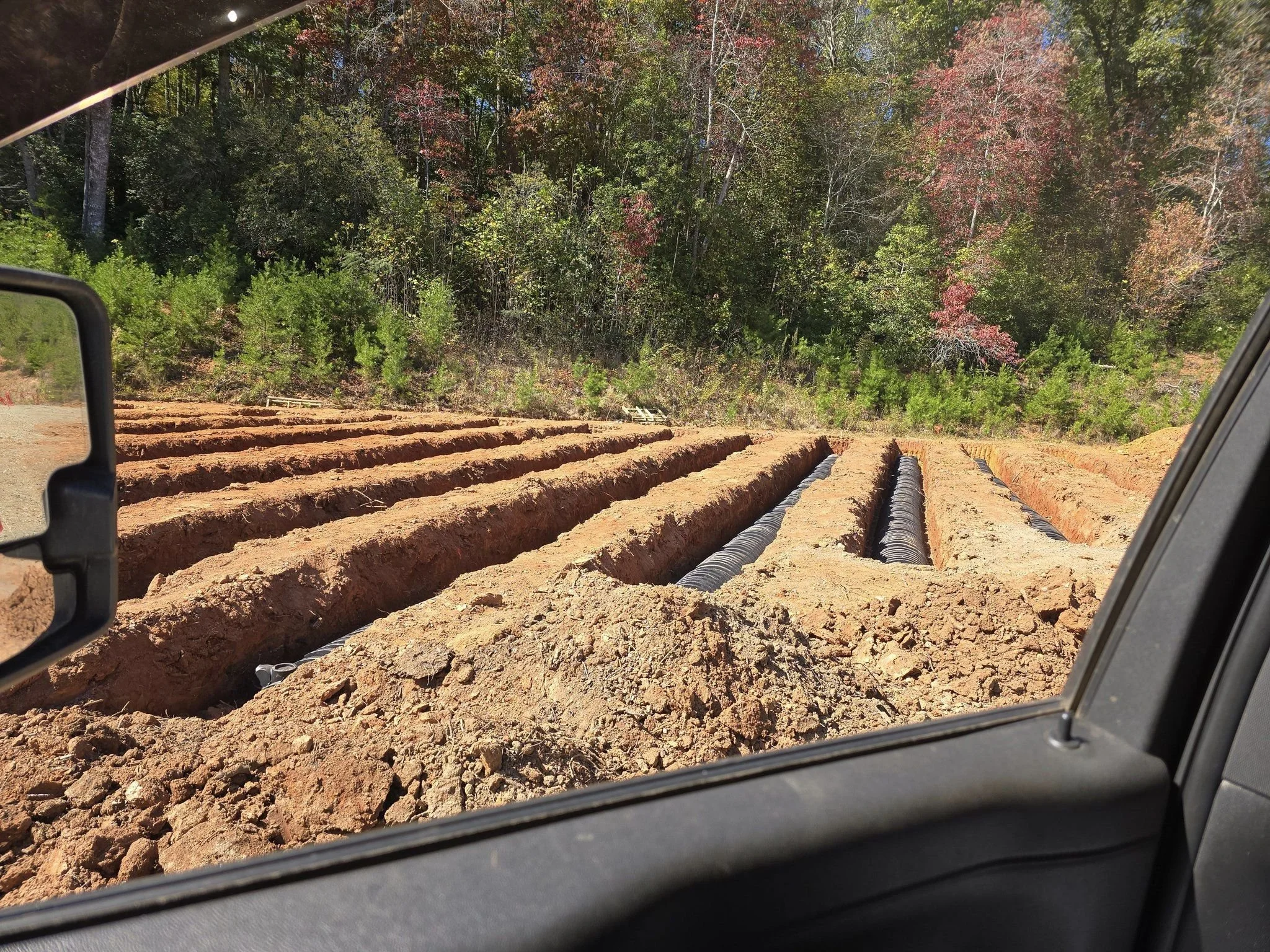 Construction site with trenches for underground pipes and trees in the background.